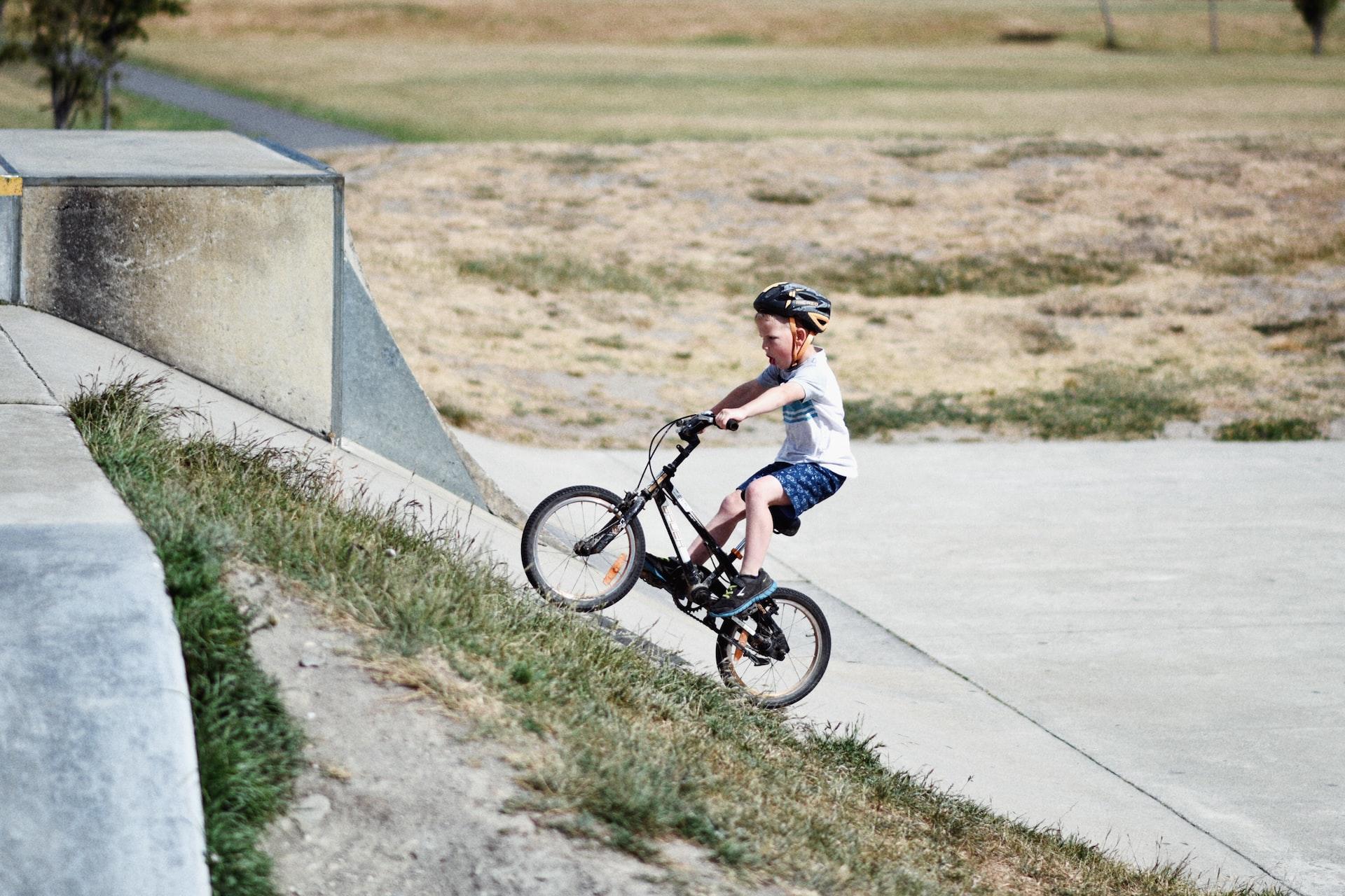 A boy wearing a grey shirt and bicycle helmet rides his bike out of a gully
