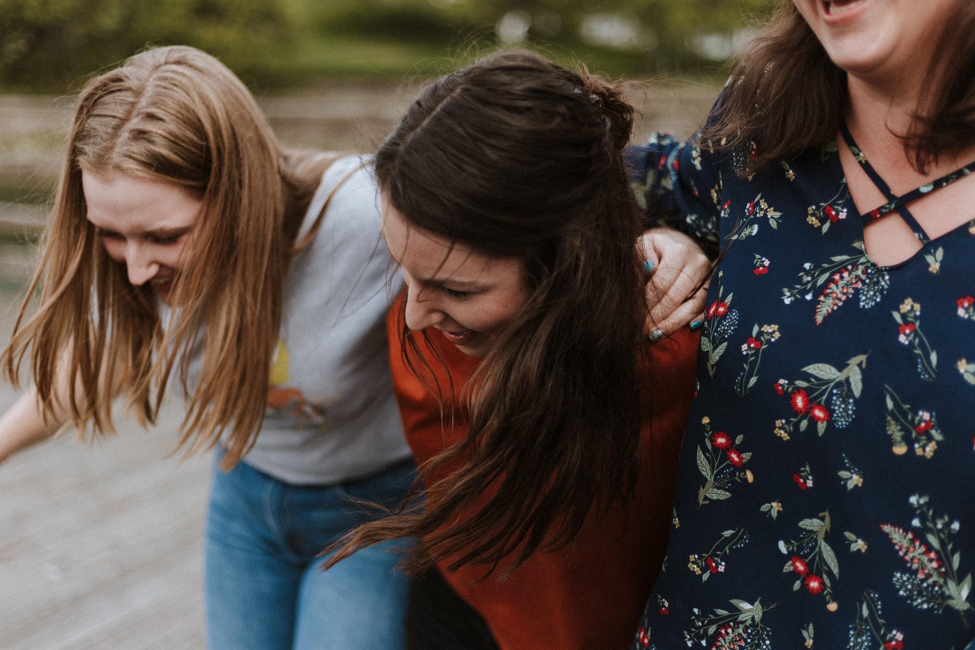 Three young women walk arm in arm, laughing heartily.