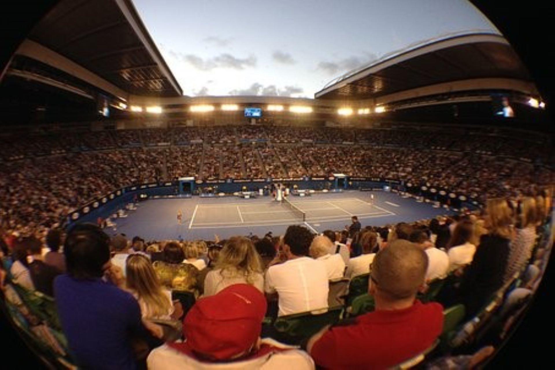 Several people watching a tennis match at a hardcourt stadium.