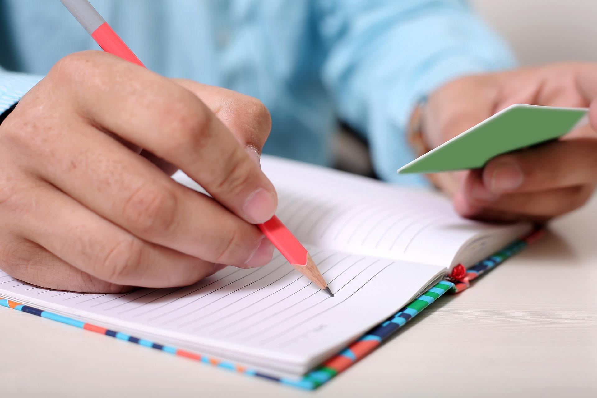 Someone taking notes and looking at a flash card 