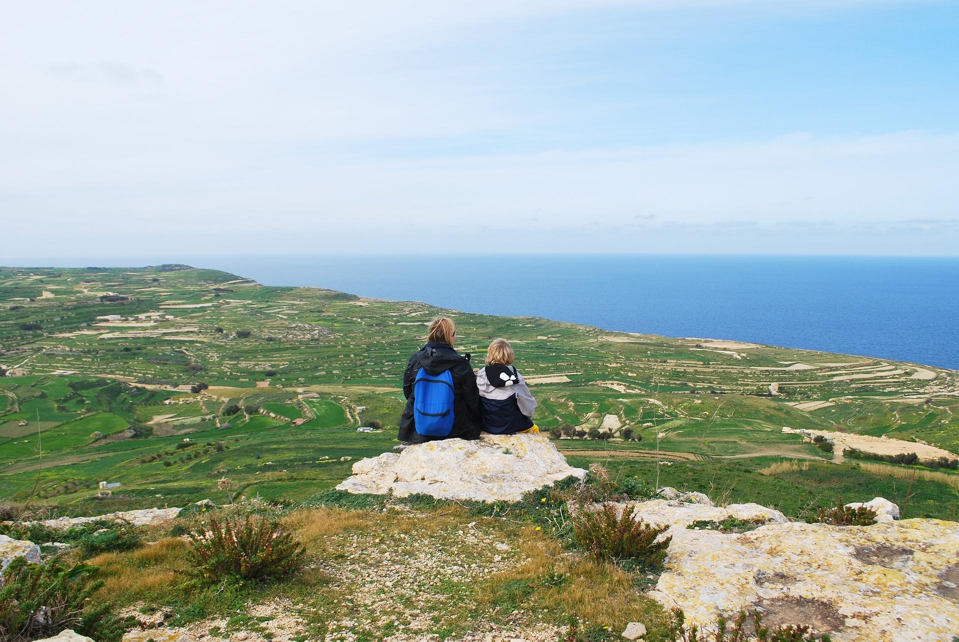 Parent and a child sitting in a cliff looking at the landscape