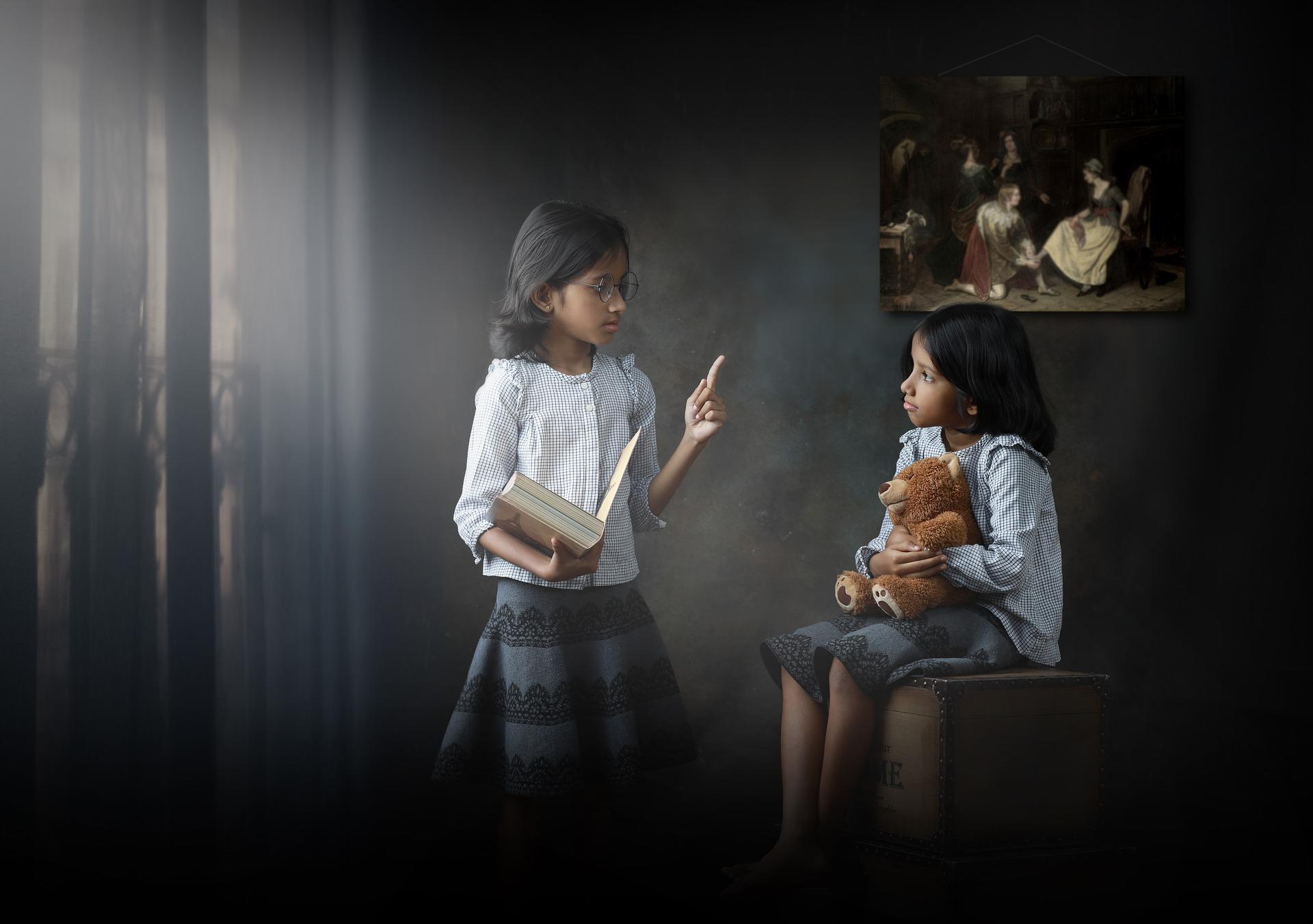 A little girl teachs another little girl with a teddy bear