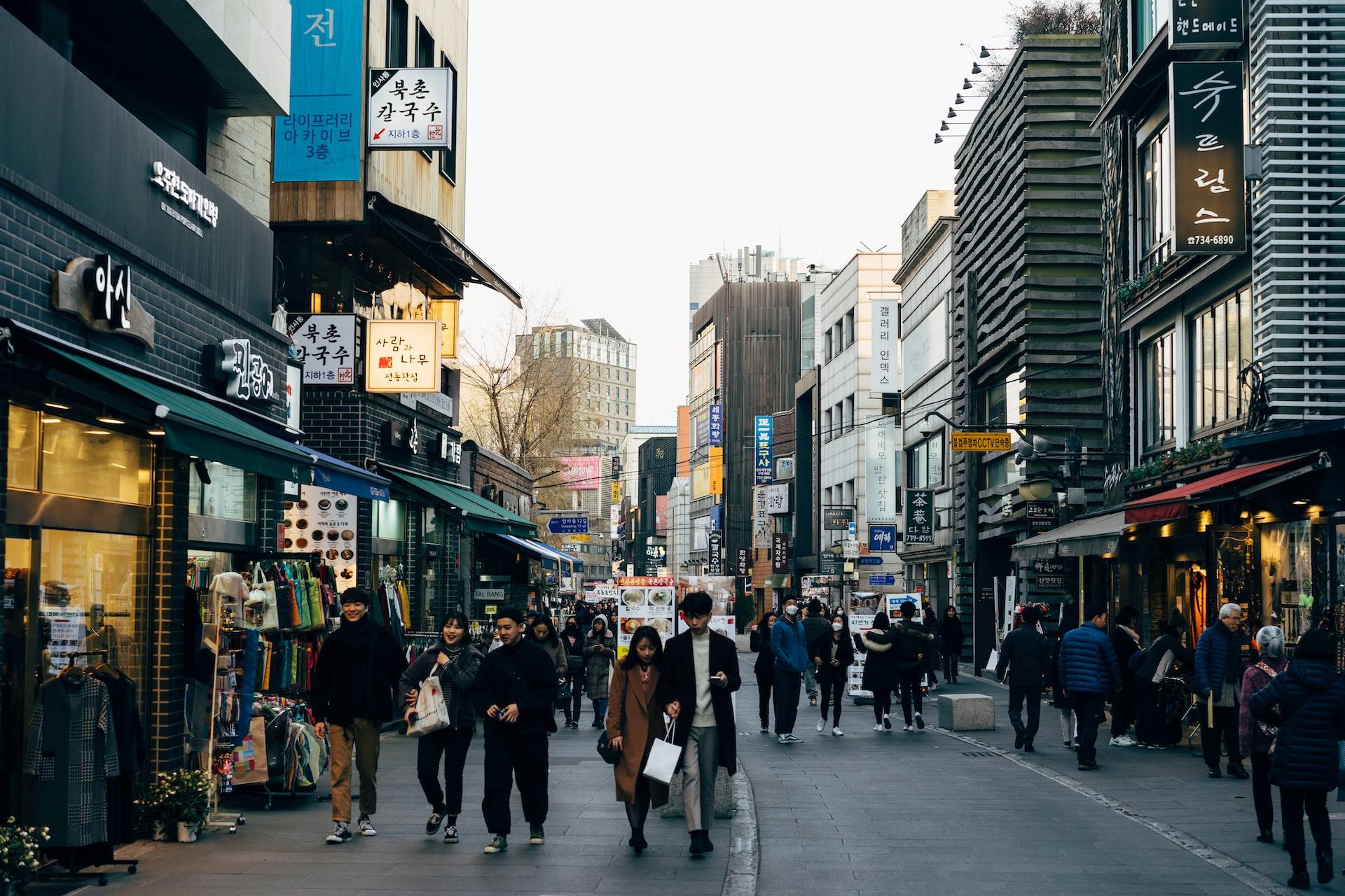 A pedestrian street in South Korea on a cloudy day with people walking and carrying shopping bags.