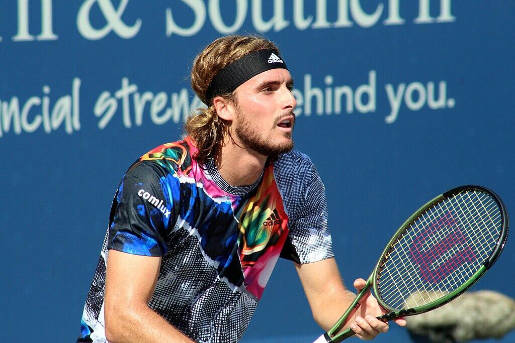 A tennis player in a colorful shirt prepares to serve on a court, with a blue backdrop featuring motivational text.