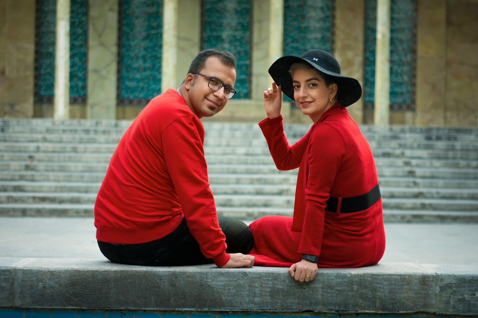 Two people wearing red, sitting on a ledge. 