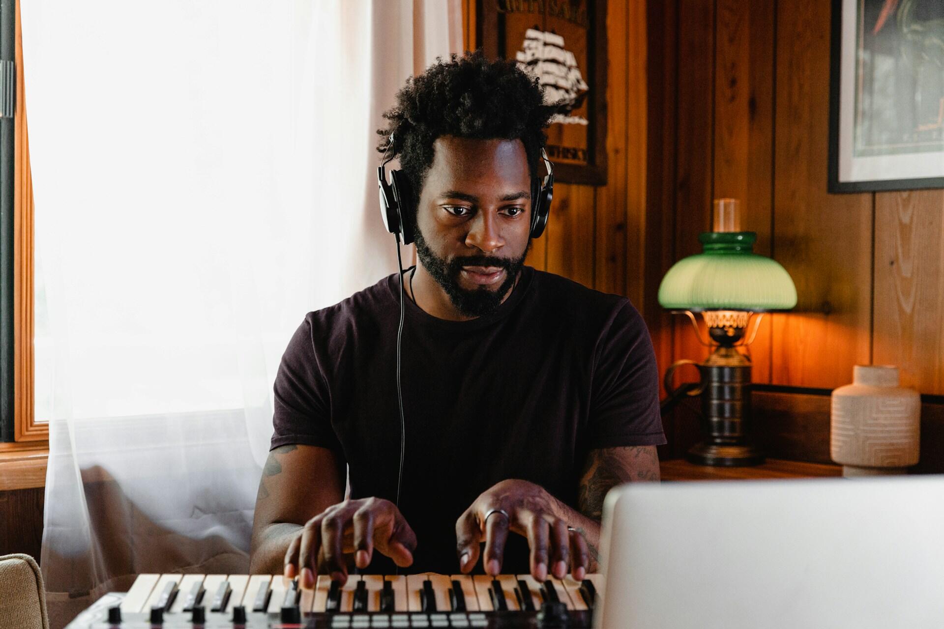 Person wearing headphones playing an electronic keyboard in a cozy room with wood paneling and soft lighting.