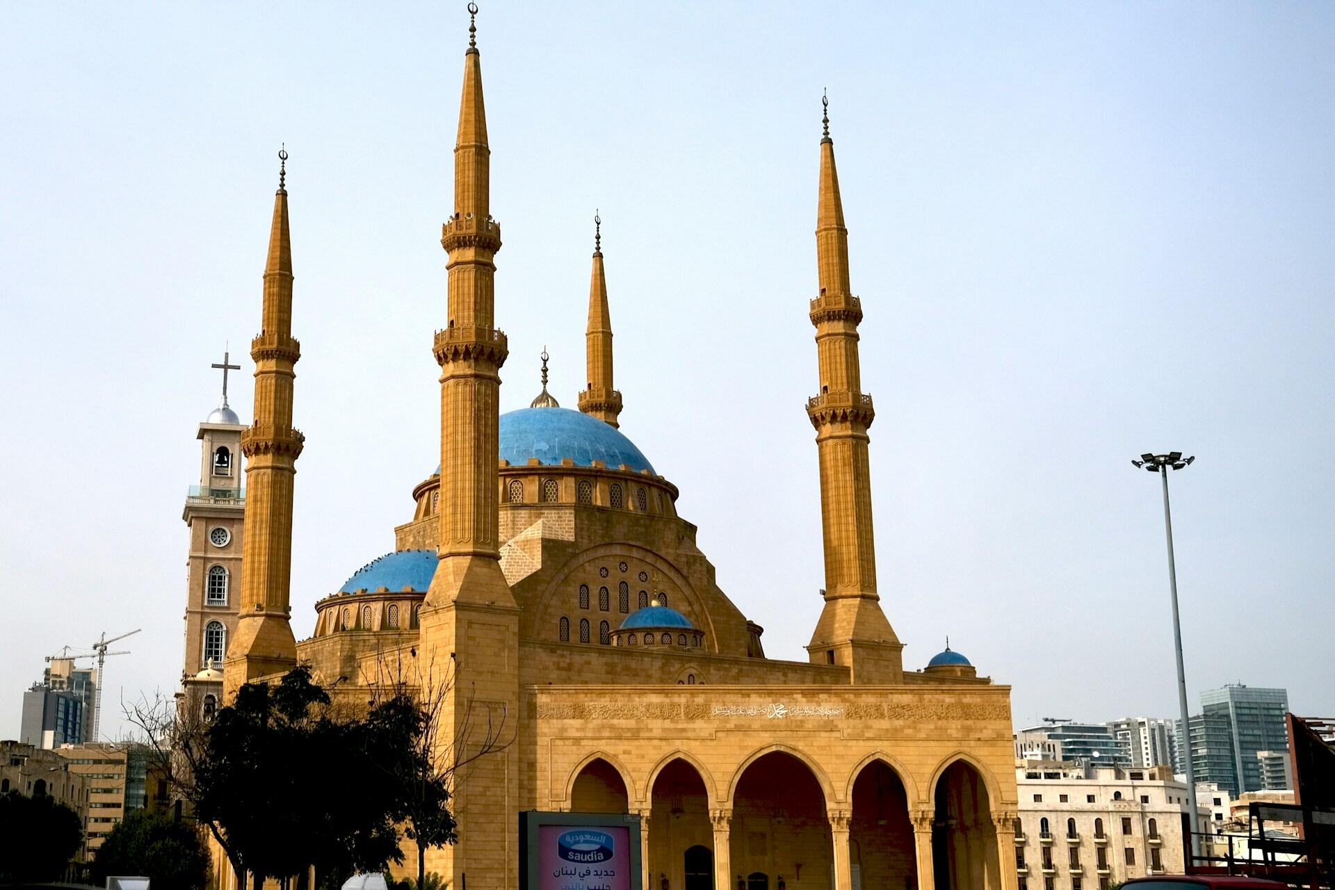 Large mosque with blue domes and tall minarets stands in an urban setting under a clear sky.
