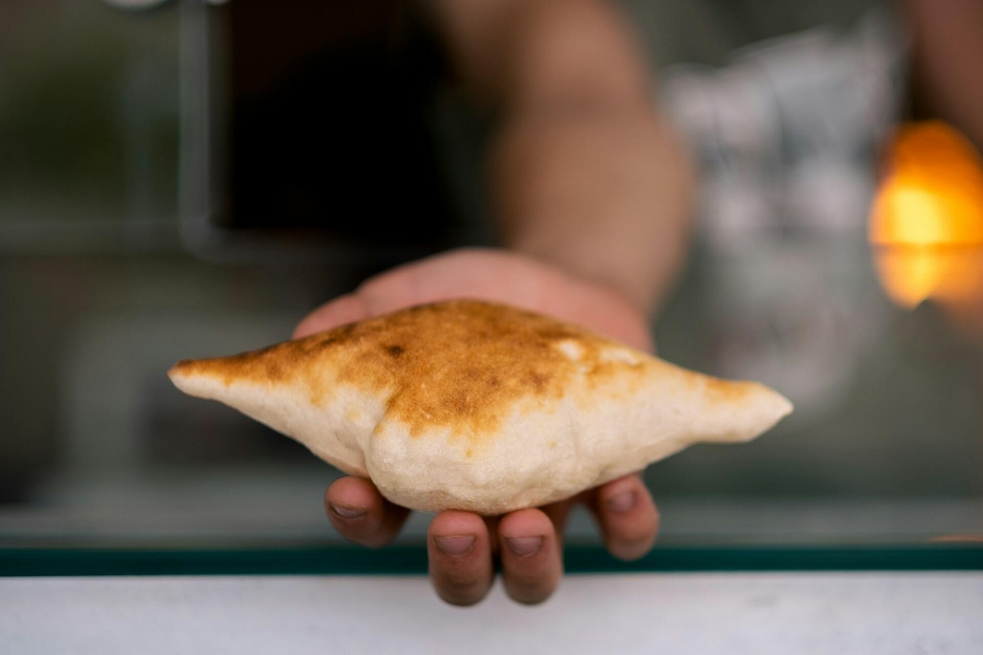 Hand holding a freshly baked, golden-brown puffed bread with a blurred background.