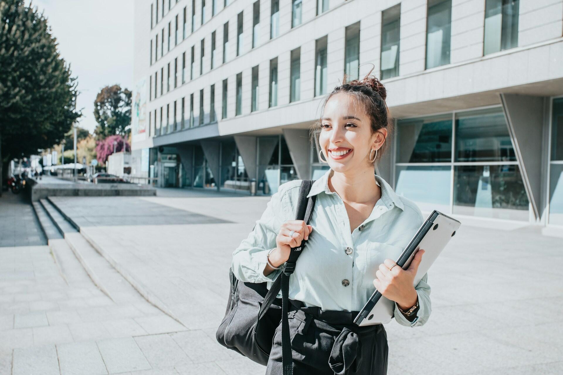 A woman with her hair up carrying books on a sunny day. 
