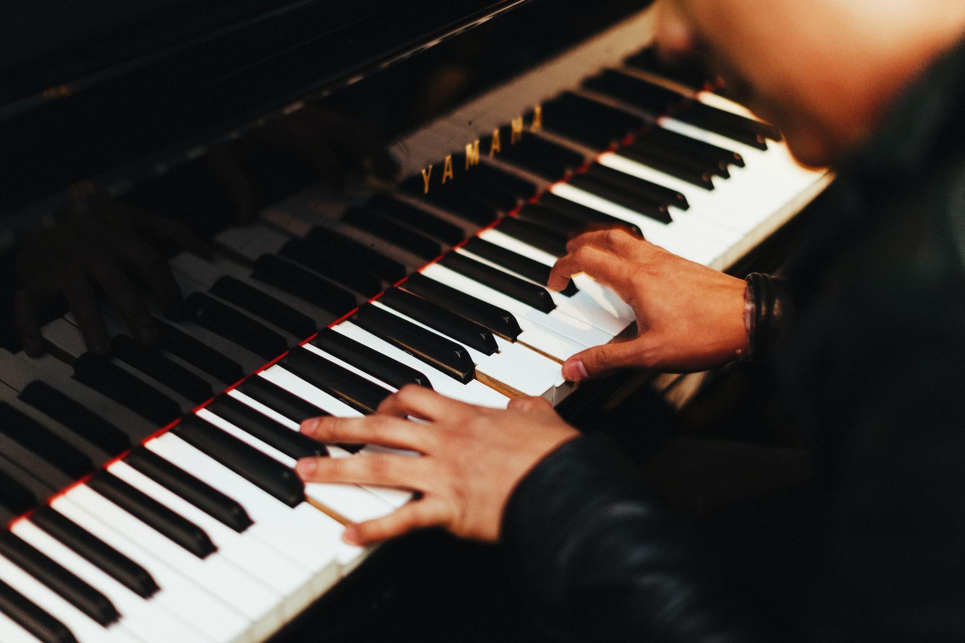 A person wearing a black top plays a piano with a black finish.