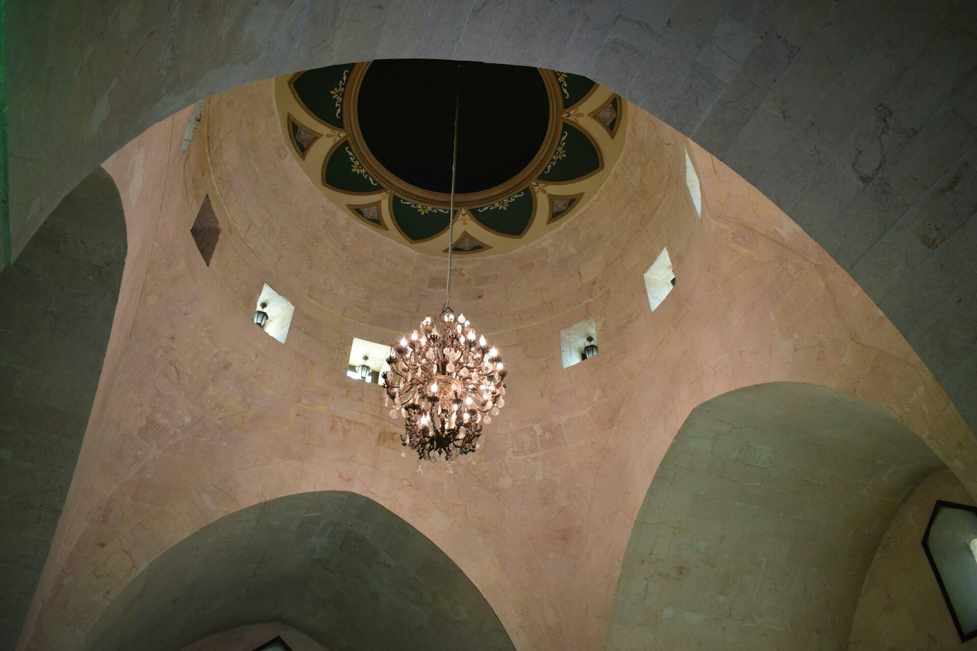 Interior view of a domed ceiling with small windows and an ornate chandelier hanging at the center.