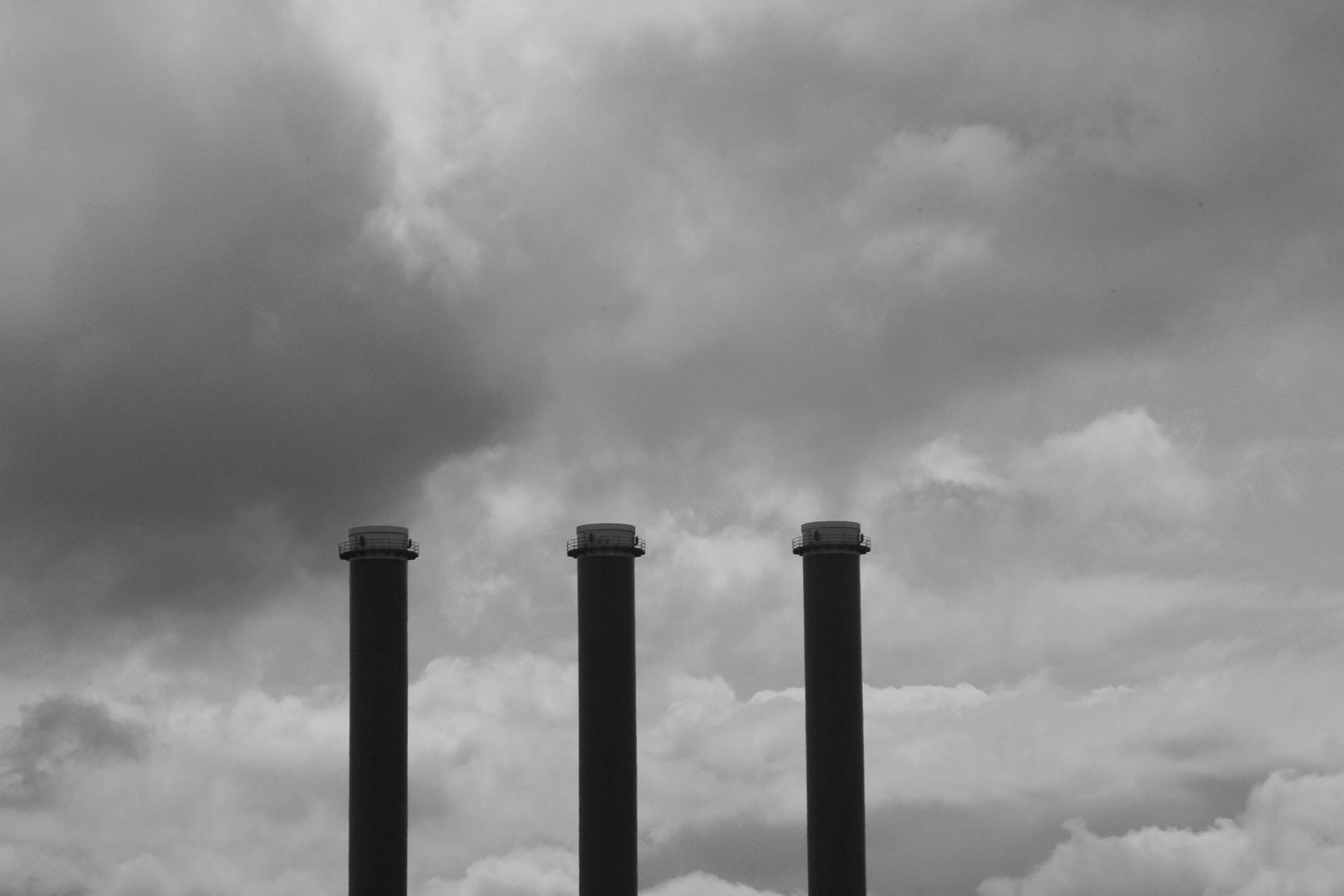 Three black smokestacks belch their contents against a hazy, leaden sky. 