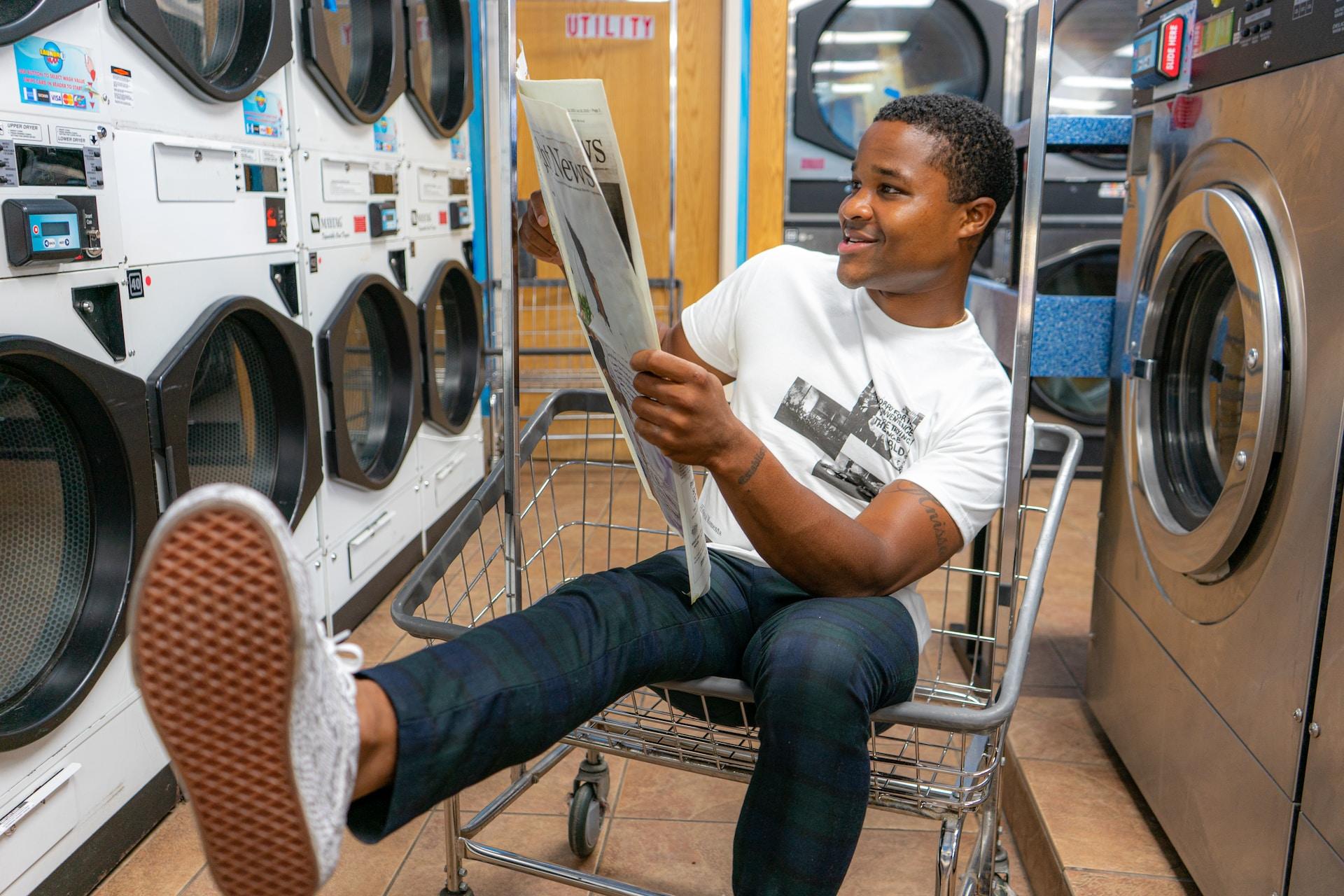 Man sitting in a laundry basket inside a launderette.