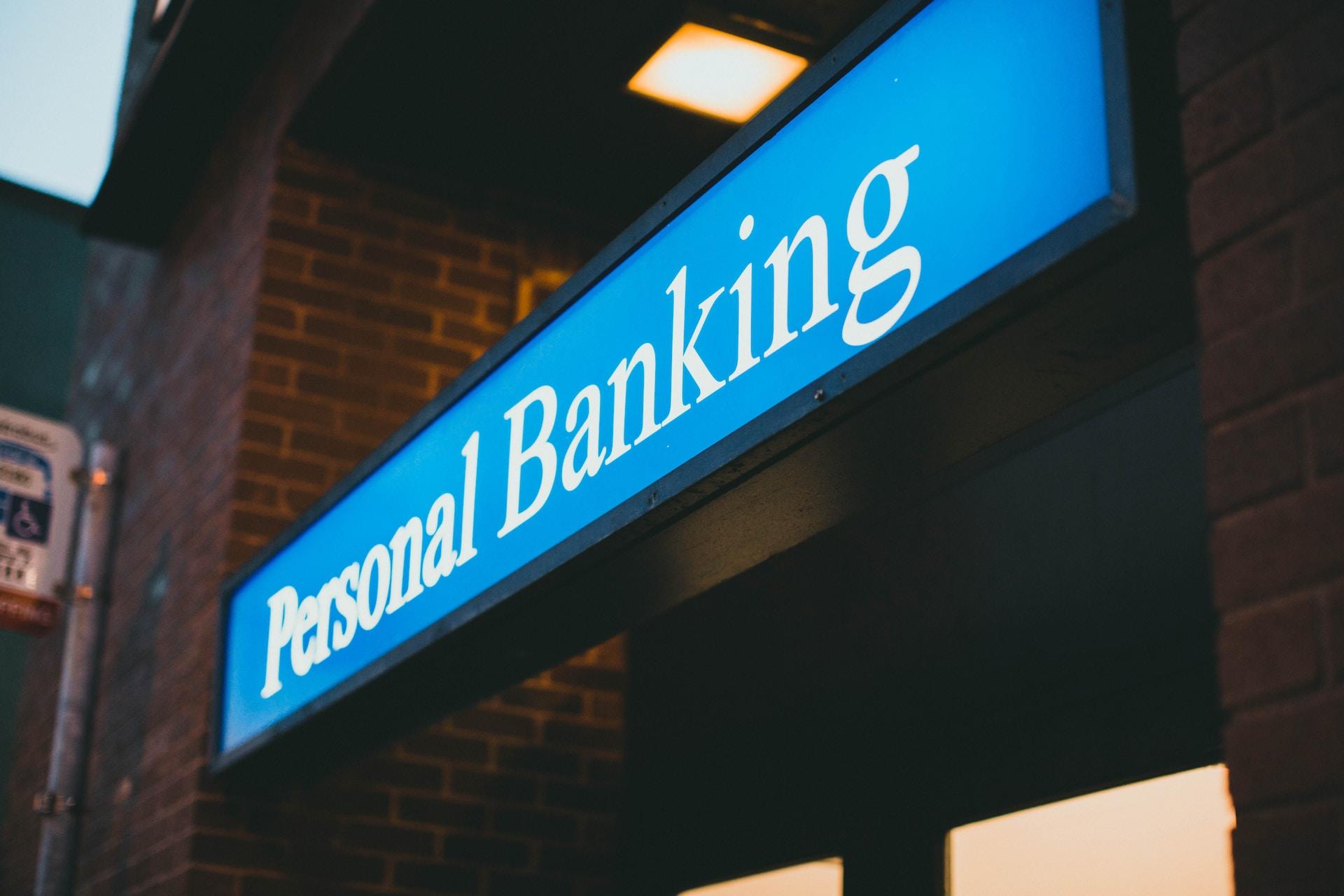 A light blue sign saying Personal Banking in white letters overhanging the entrance to a brick building.