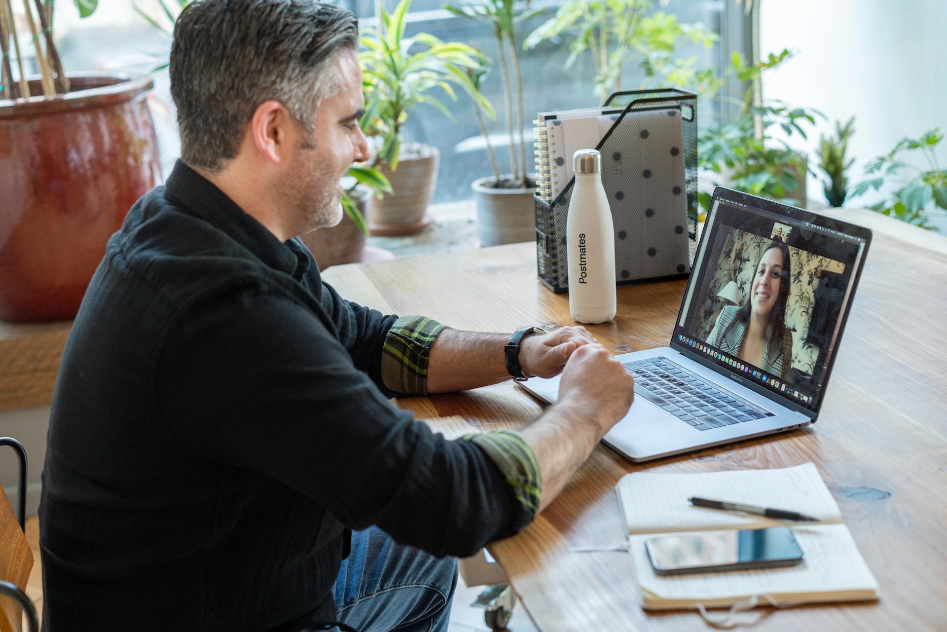 A man is talking to a woman on video on a laptop in front of him.