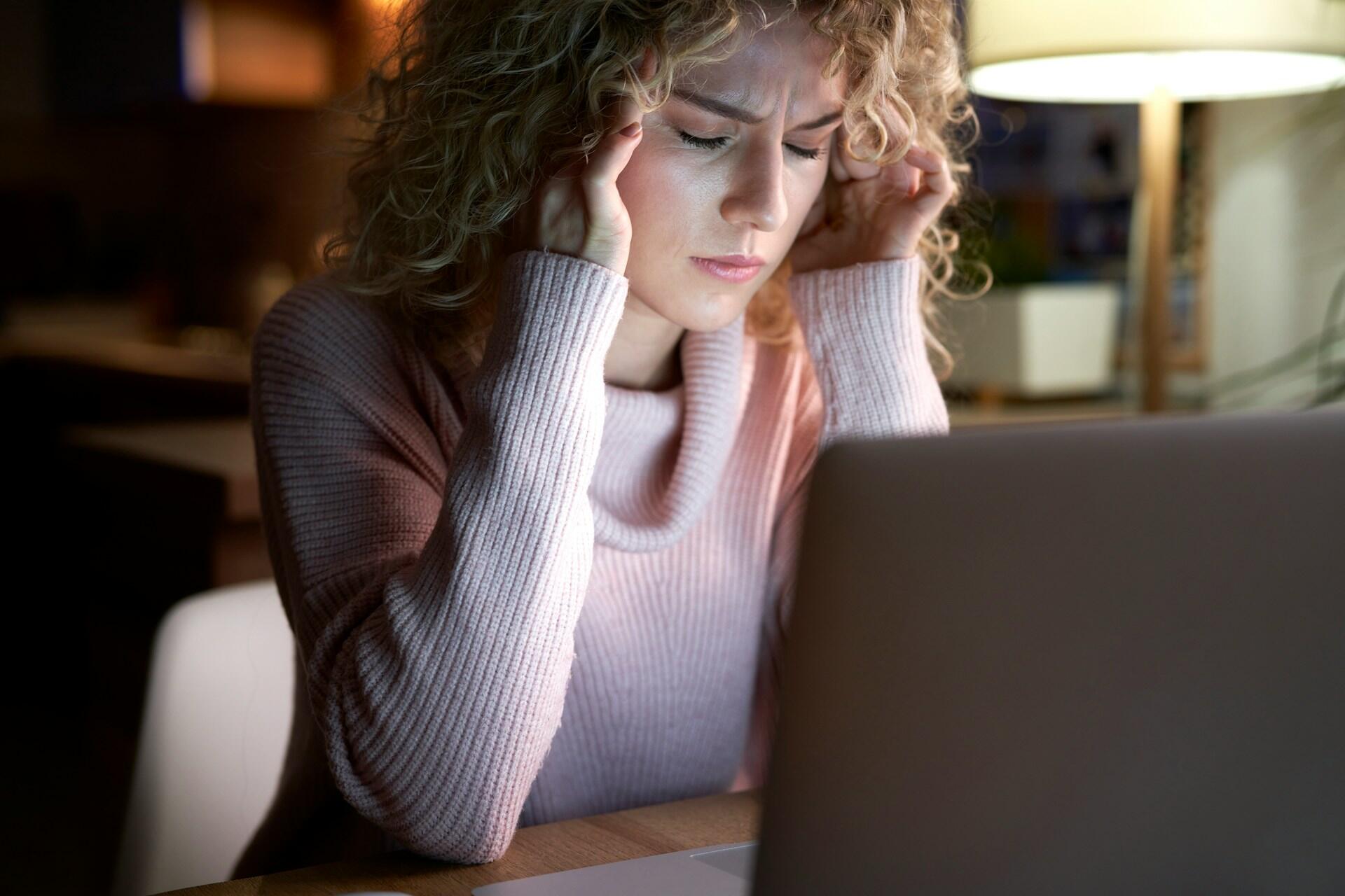 A woman in front of a laptop with her hands massaging her temples.