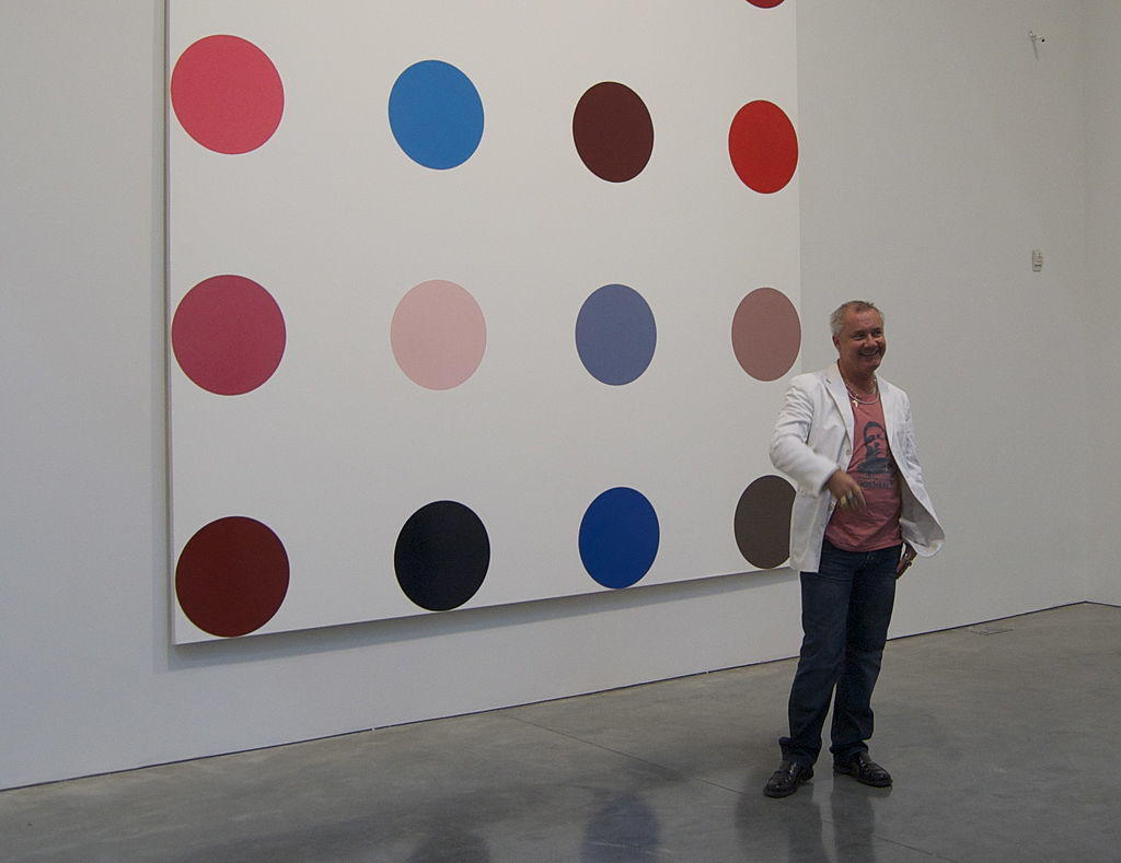 Damien hirst standing in front of painting