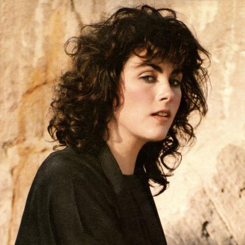 Laura Branigan wearing black and standing in front of a dusty background.