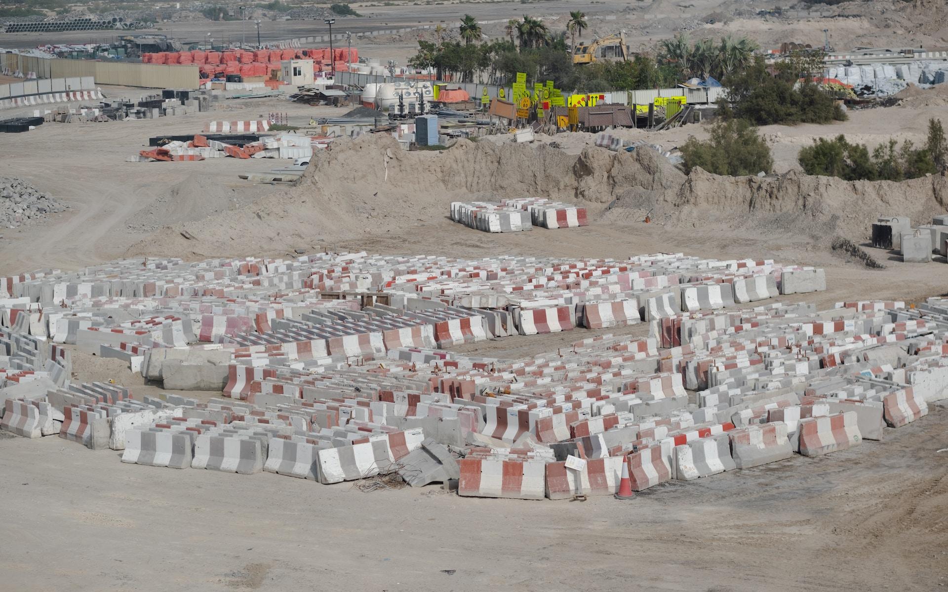 A collection of red and white construction barriers in the desert, arranged in no particular fashion, with construction outbuilding seen in the background.