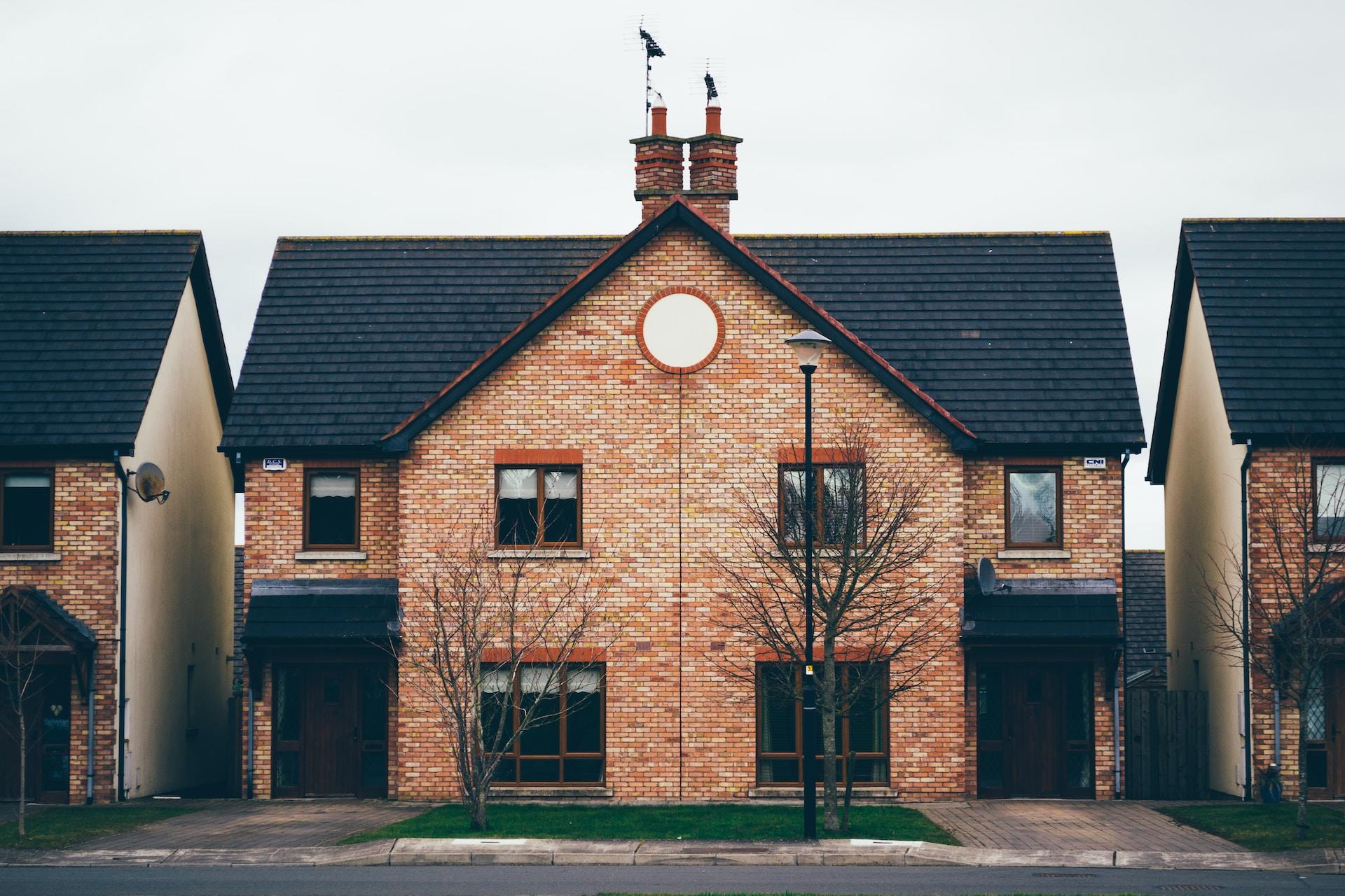 A duplex house with black tarpaper roof and red brick, with large windows on the ground floor and smaller ones atop and the driveway lined up with each home's entrance.