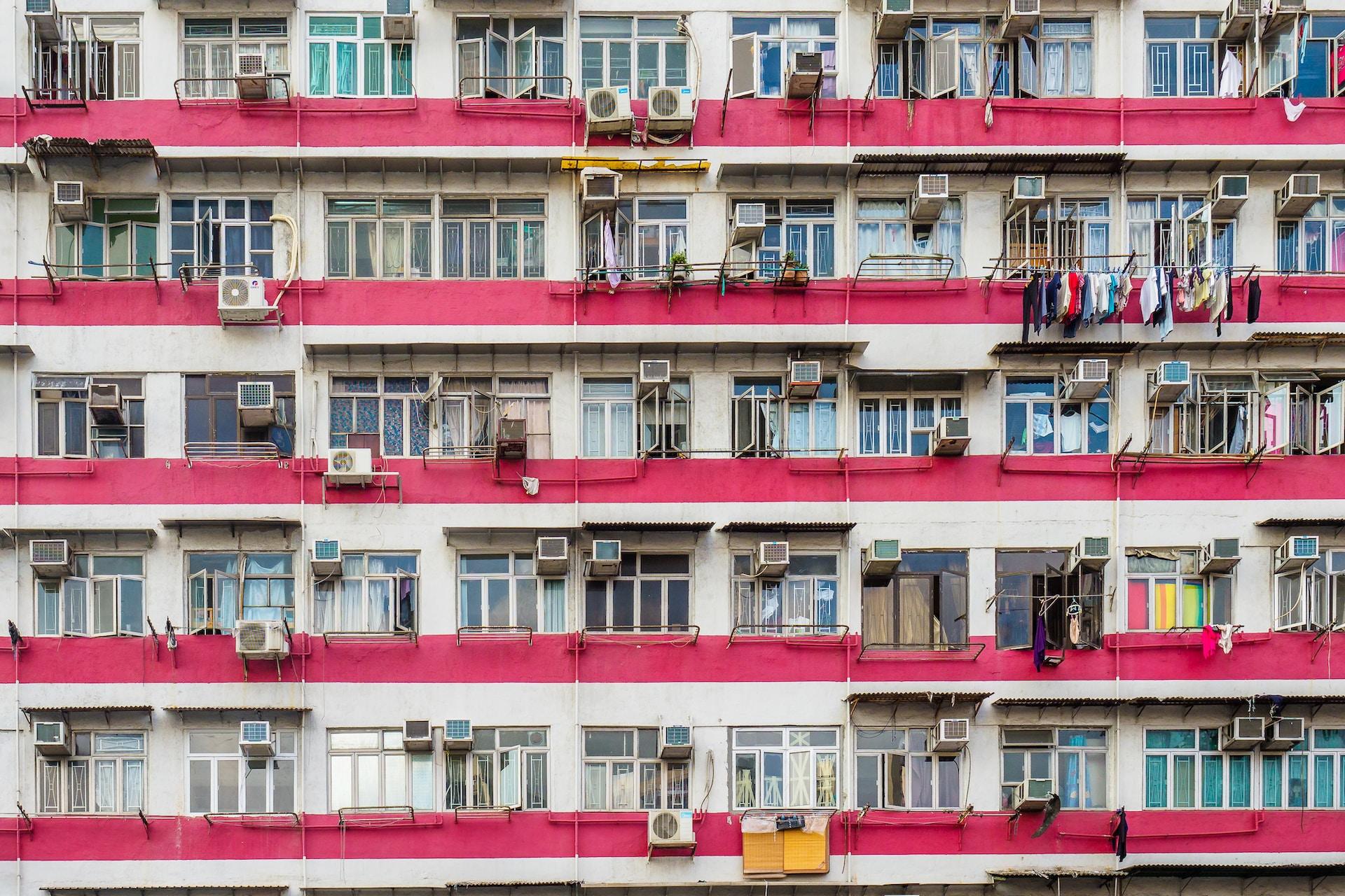 A section of a housing block painted white with pink stipes to mark the different levels. The facade bears many windows and air conditioners