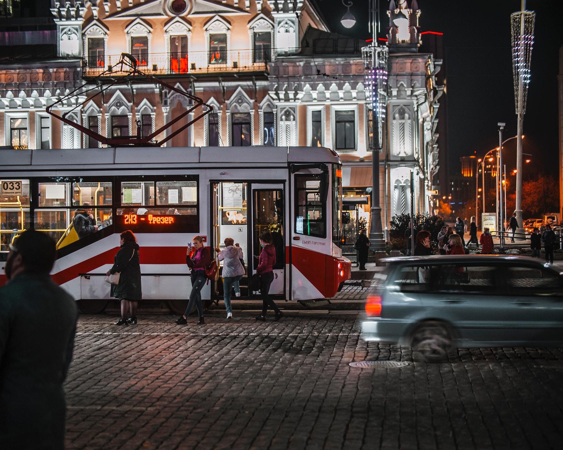 Yekaterinburg at night, with a red and white tram welcoming passengers in front of an orange and white imposing structure. 