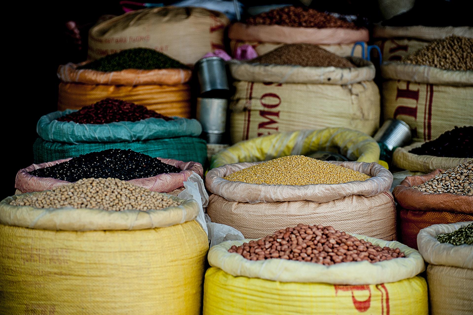 Yellow wholesale sacs of dry goods like yellow corn and black beans, with their tops rolled open and the products ready for sale. 