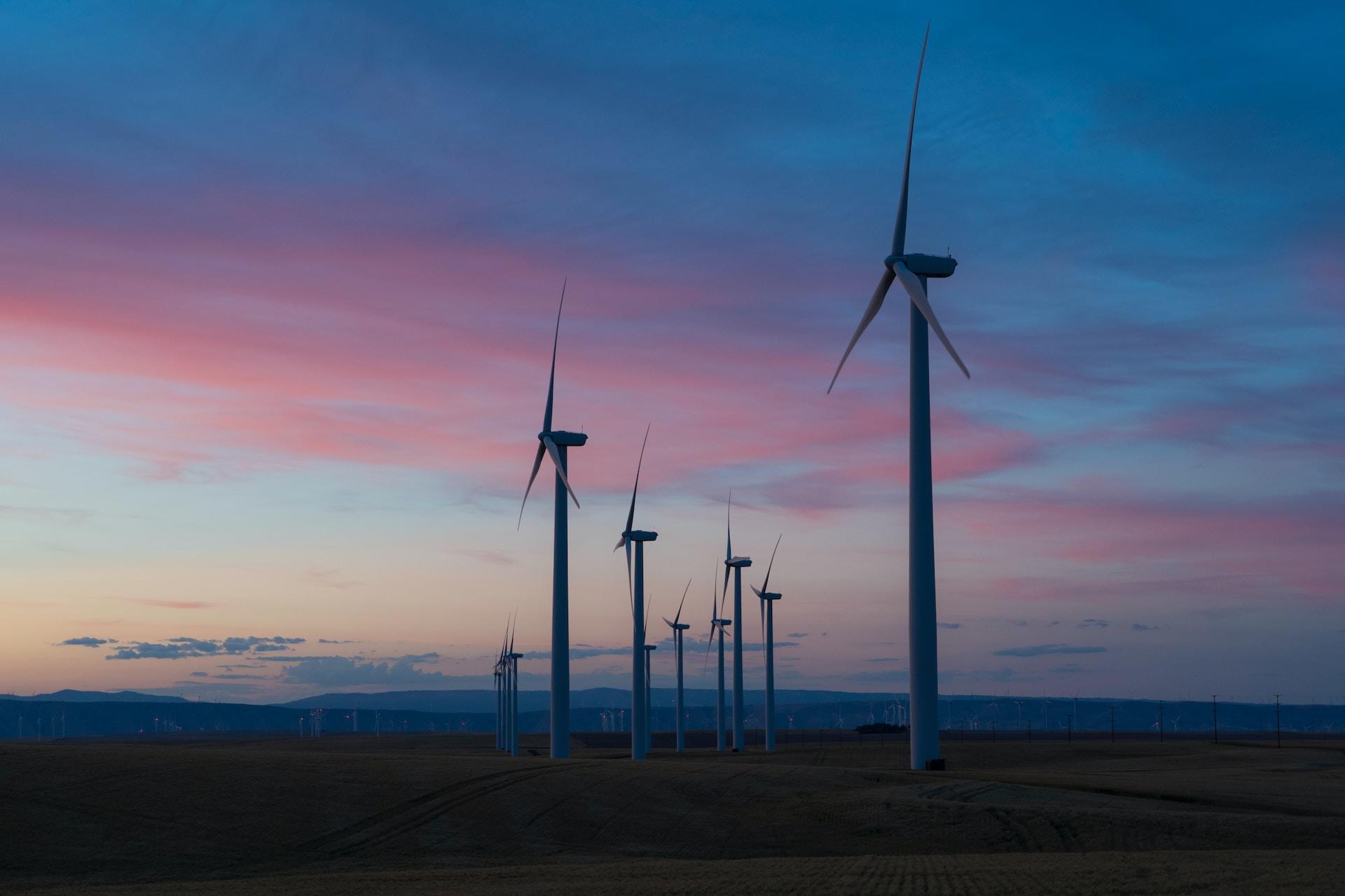 A wind farm at dusk, with an array of turbines on level ground set against an indigo and pink sky.