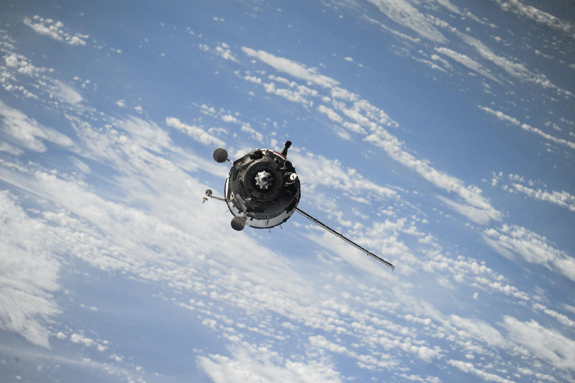 A space vehicle suspended against a blue sky streaked with clouds.