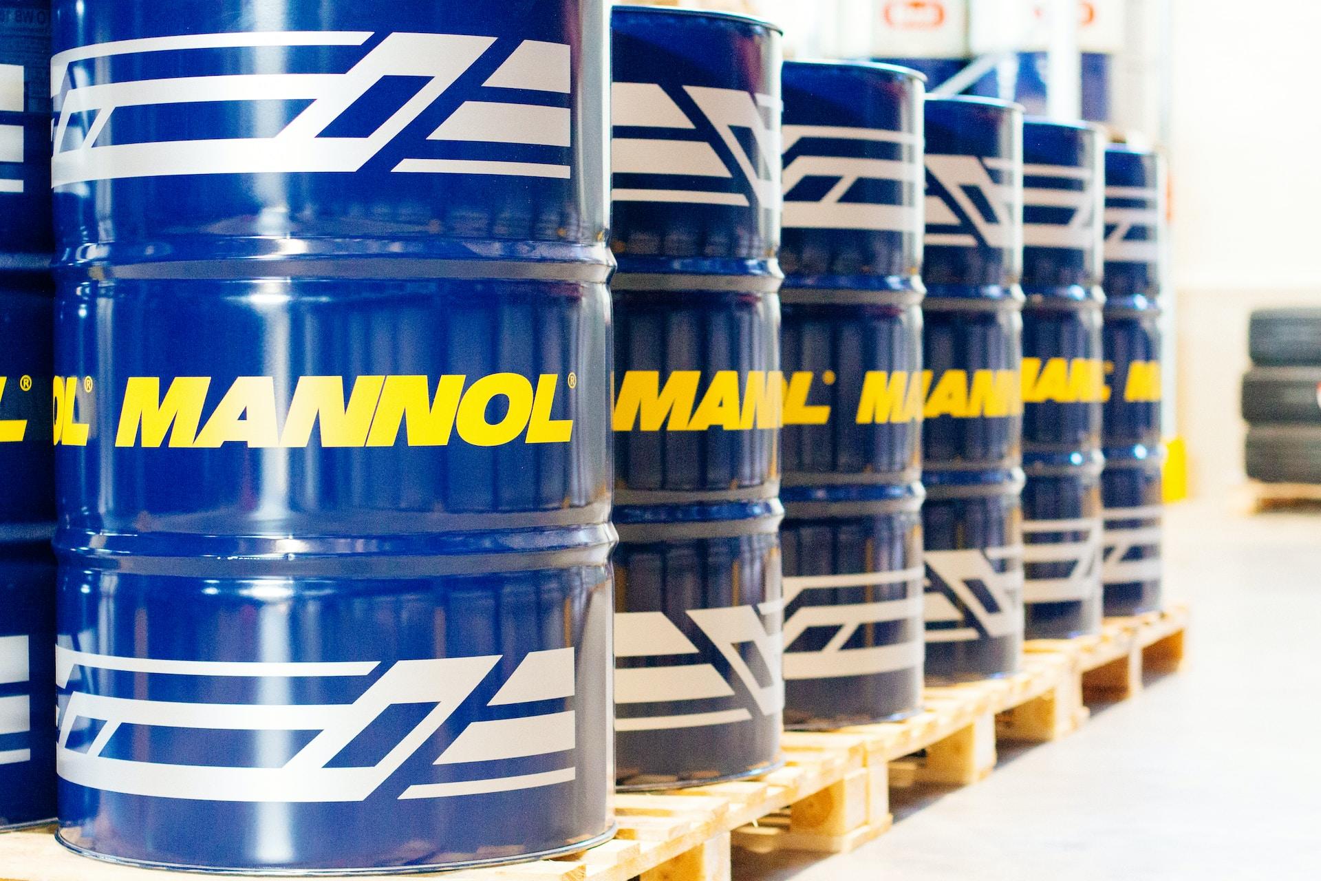 Six blue oil drums with a white frieze painted on their upper and lower thirds, with the word Mannol written in yellow occupying the middle third. 