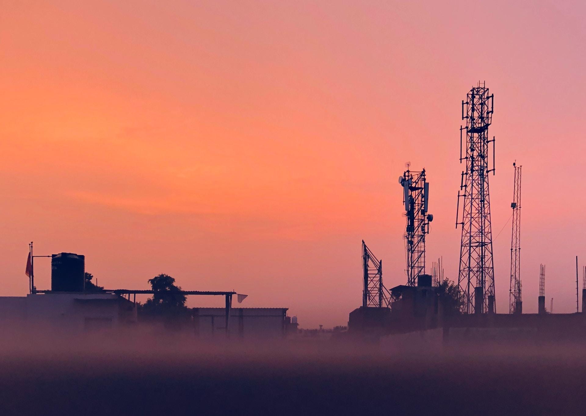 A refinery's stacks set against an orange sunset sky.