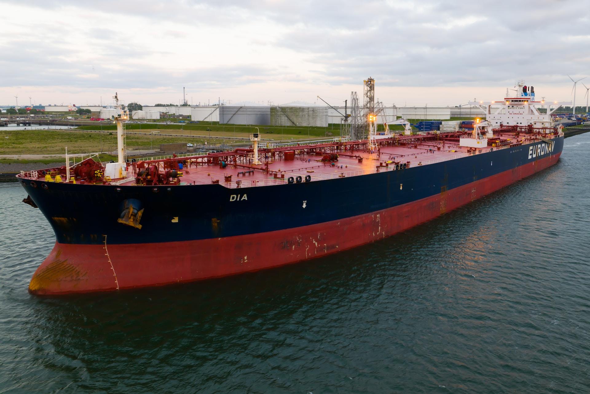 A red and black tanker prepares to leave the oil storage facility under cloudy skies.