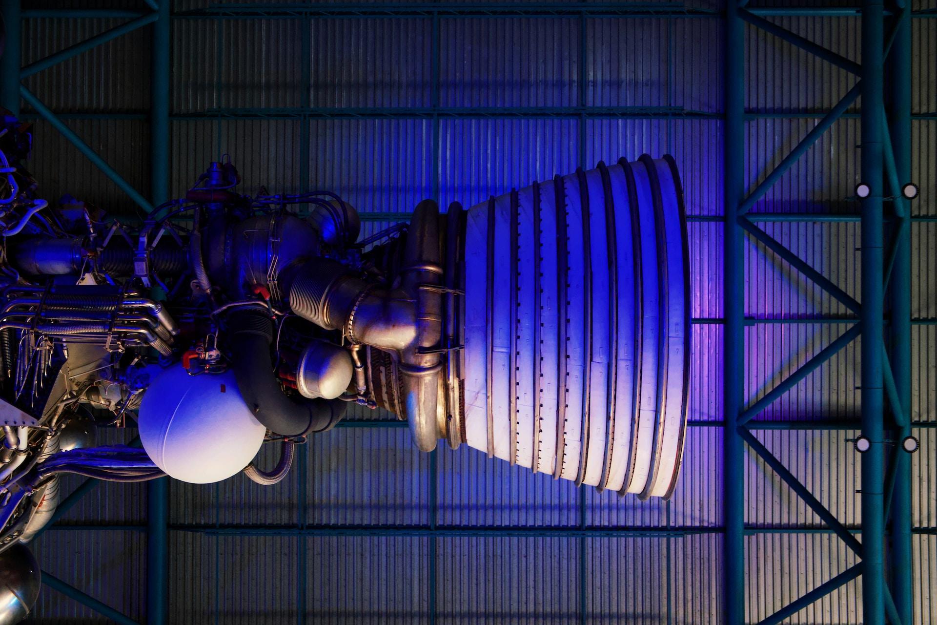 a museum display of a rocket engine from the Saturn V bathed in a purplish light.  