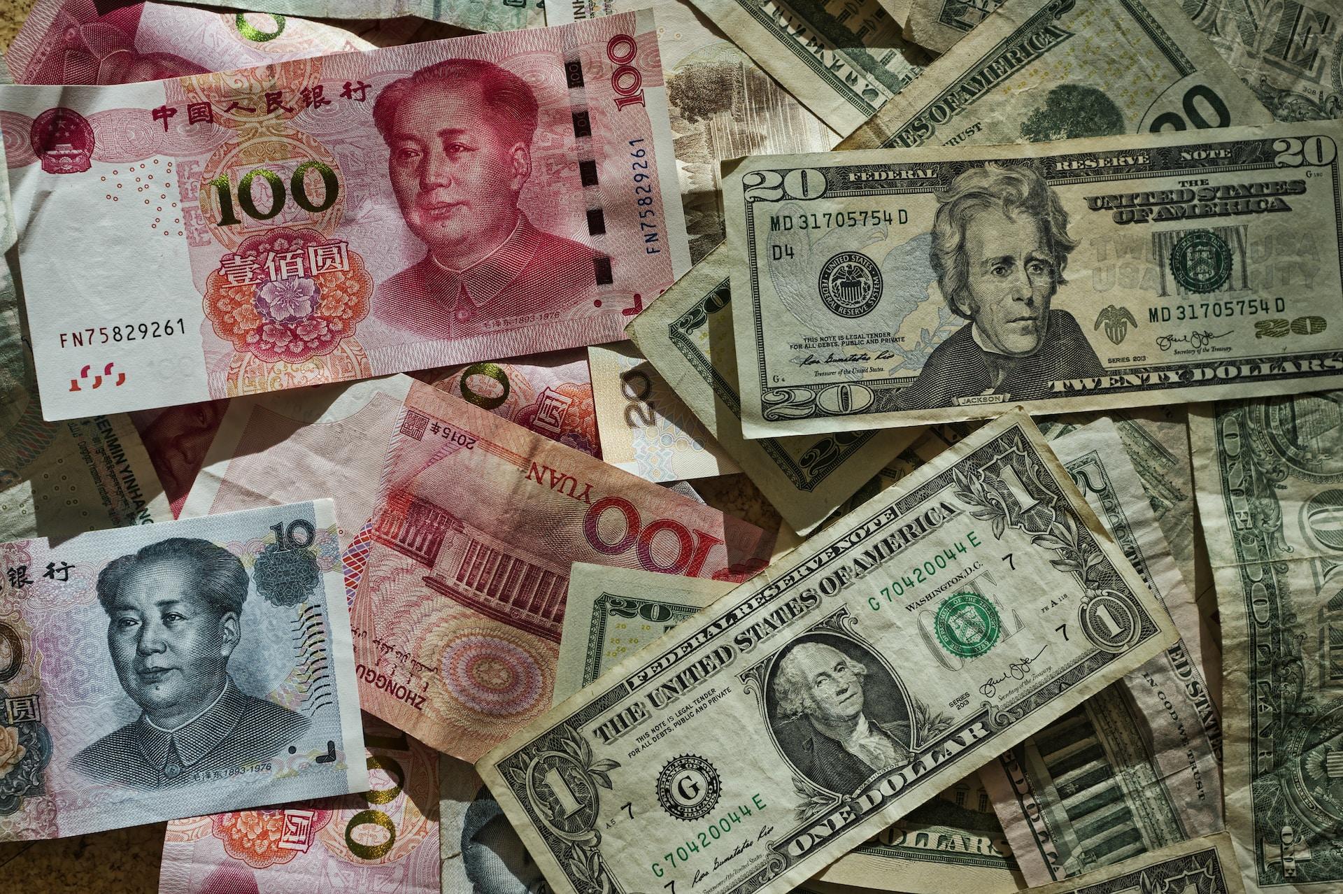 A scattered piled of red and white 100-yuan notes and green and white dollar notes in various denominations. 