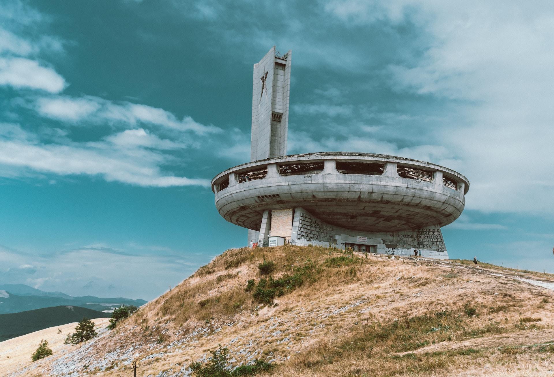 An abandoned, round concrete structure resembling a UFO perched atop a sandy hill. 