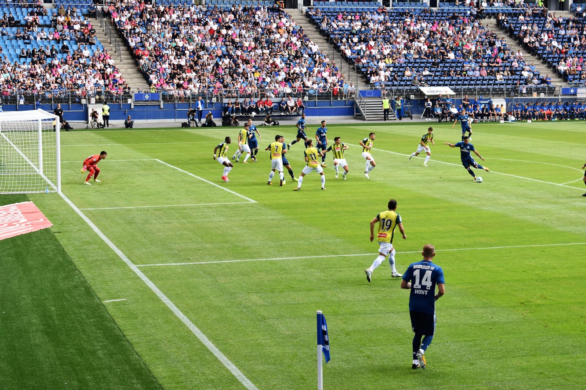 A long view of a soccer pitch with spectators in the stands visible in the background. 