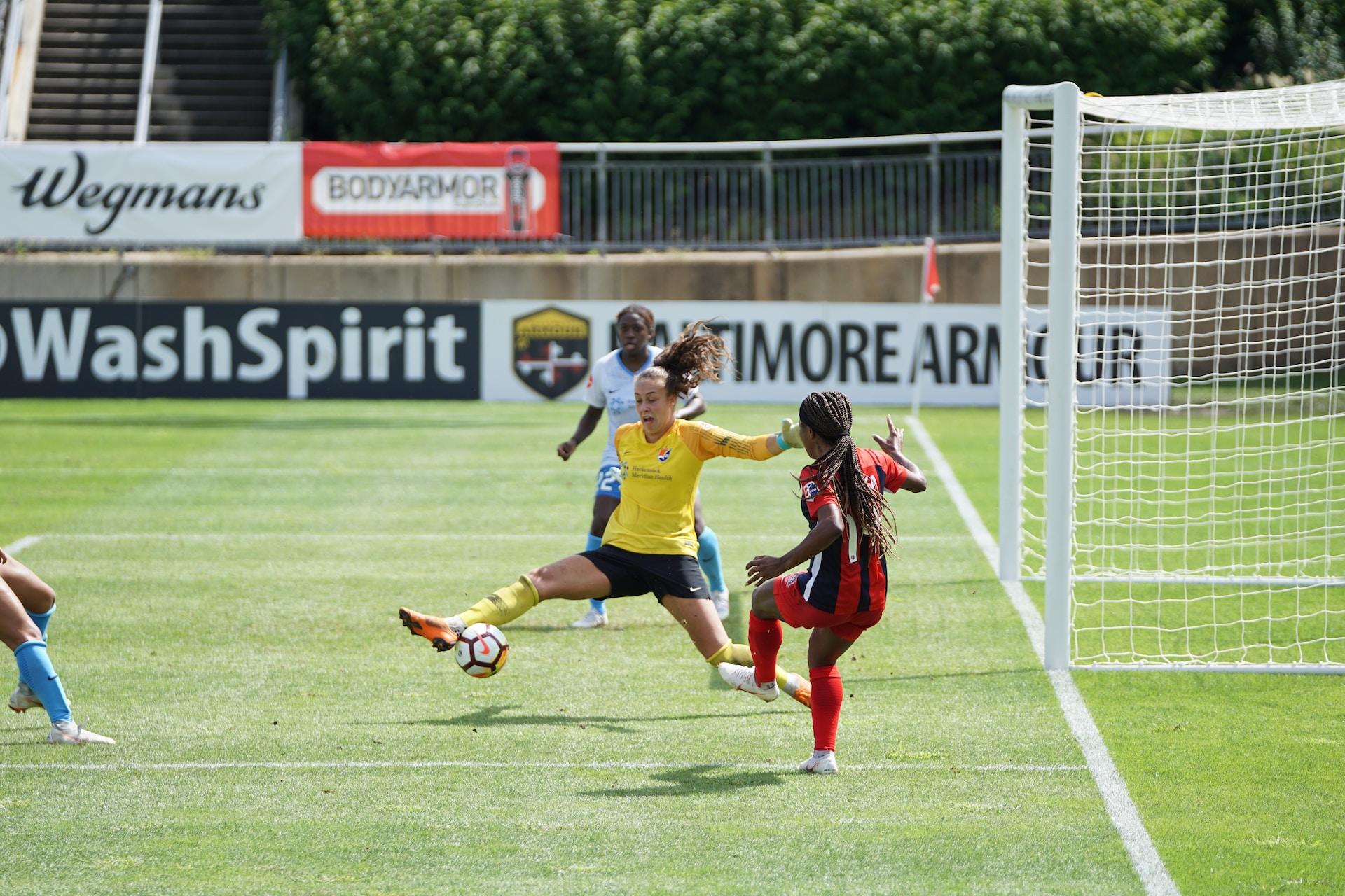 A female goalkeeper blocking a shot during a match.