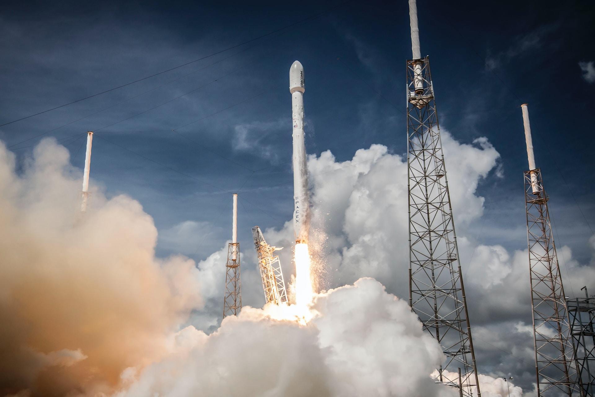 A SpaceX rocket launches, leaving clouds of exhaust in its wake.