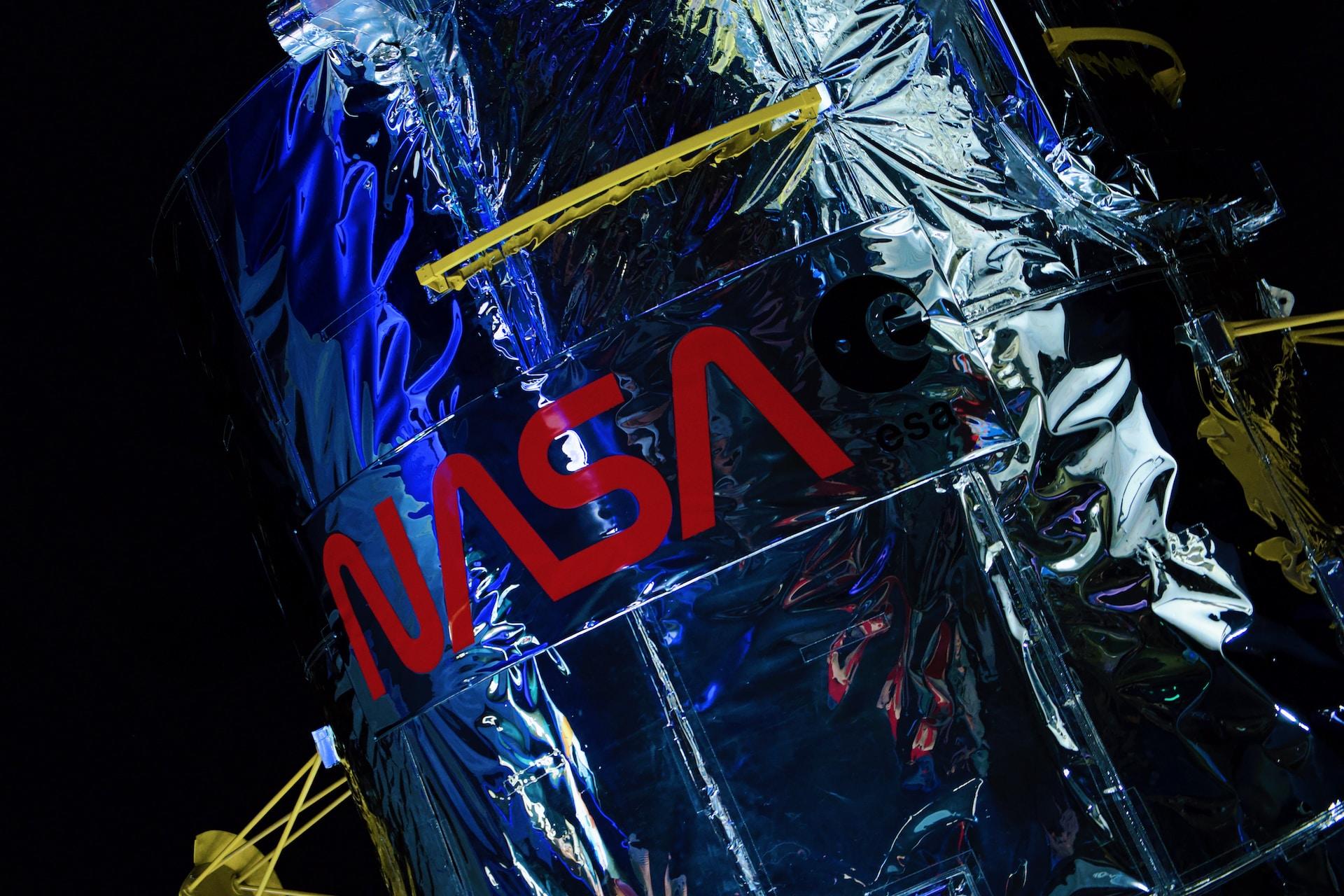 A royal blue spacecraft sheathing with NASA printed on it in bright red under a gold strip with black-lettered writing on it.  