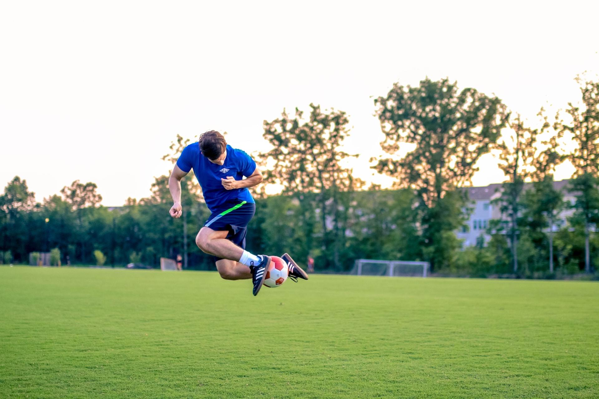 A soccer player wearing a royal and navy blue uniform leaps into the air to display his ball skills.