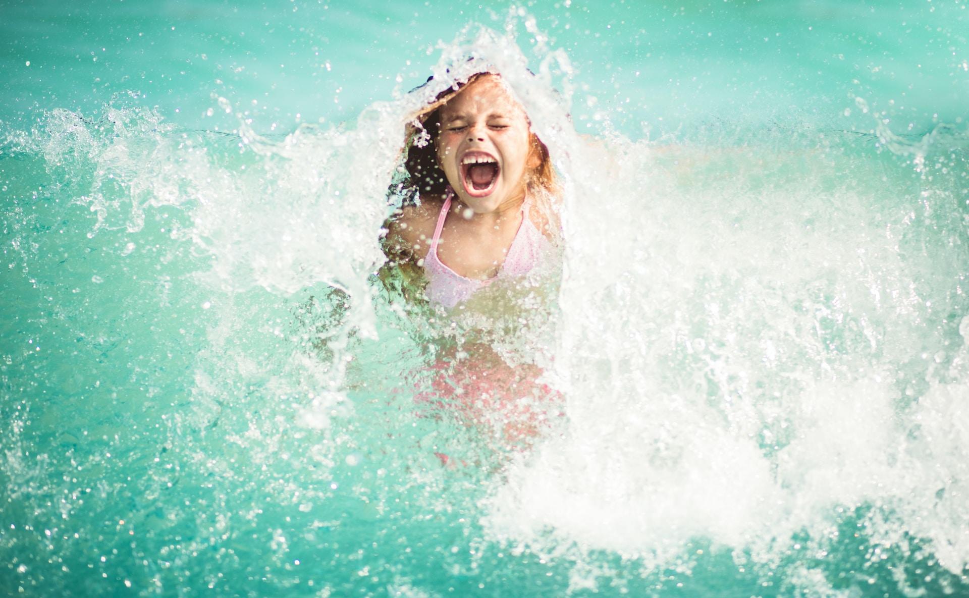 A person in a swimming pool screams as they are surrounding by splashing water. 