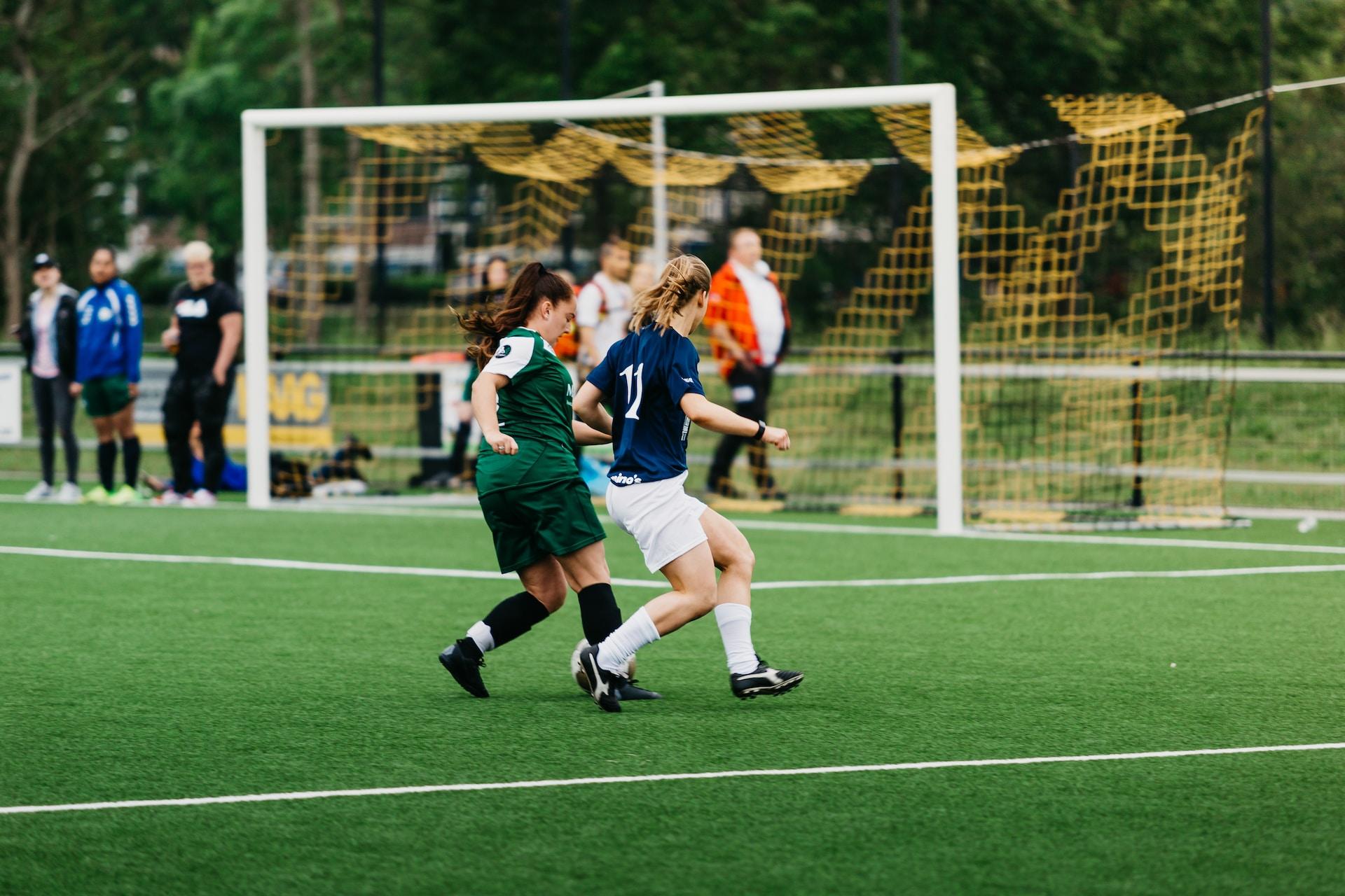 A women's soccer game in progress, one team in a navy blue and white uniform and the other wearing green and black.