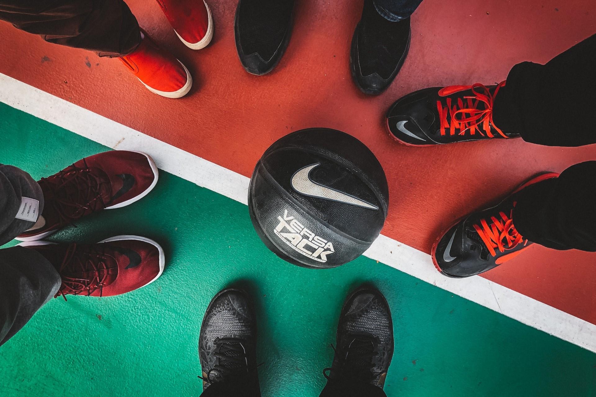 A basketball on the floor surrounded by people's feet.