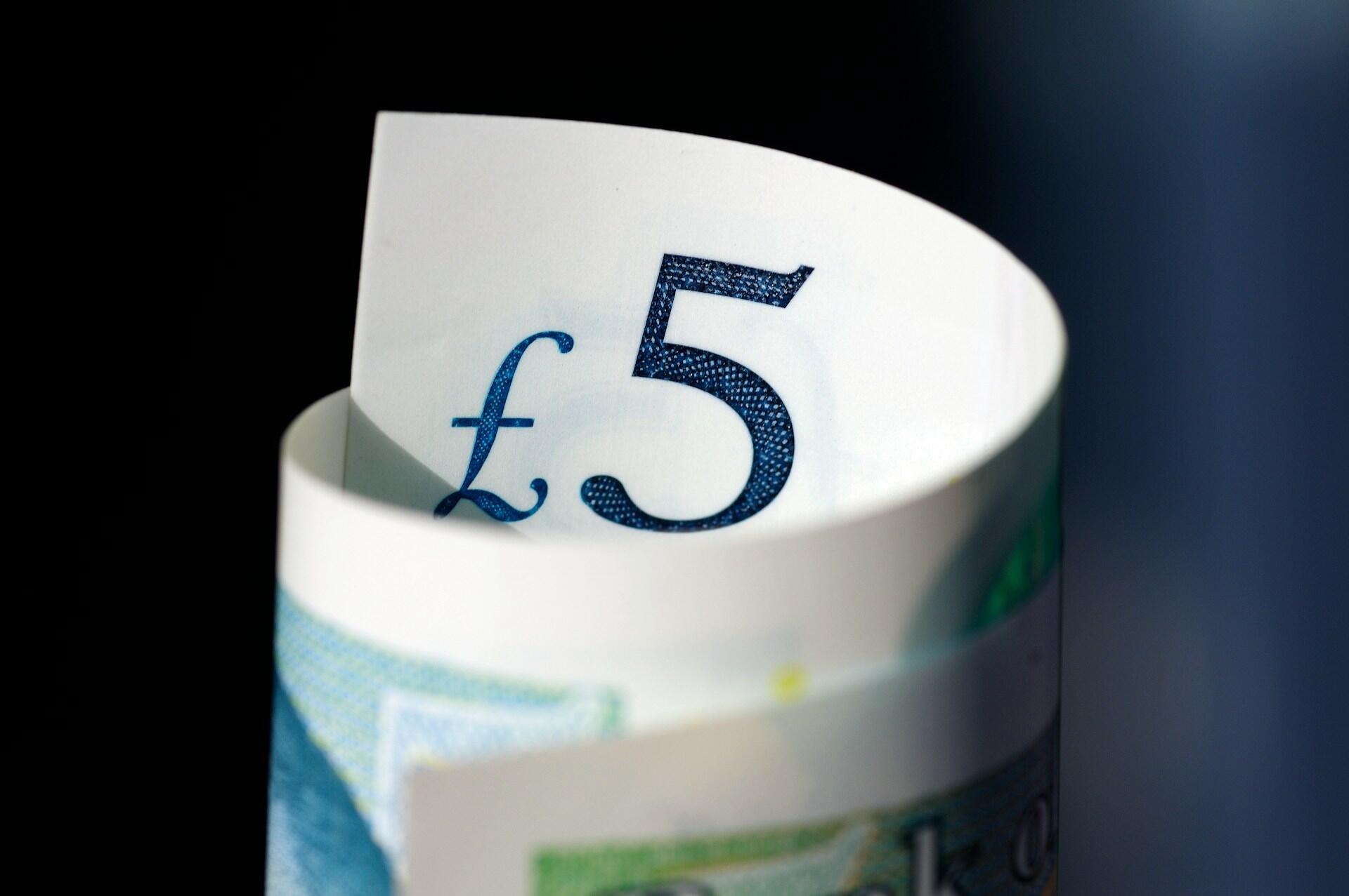 A closeup of a 5-pound note curled up lengthwise, so that the £5 shows.