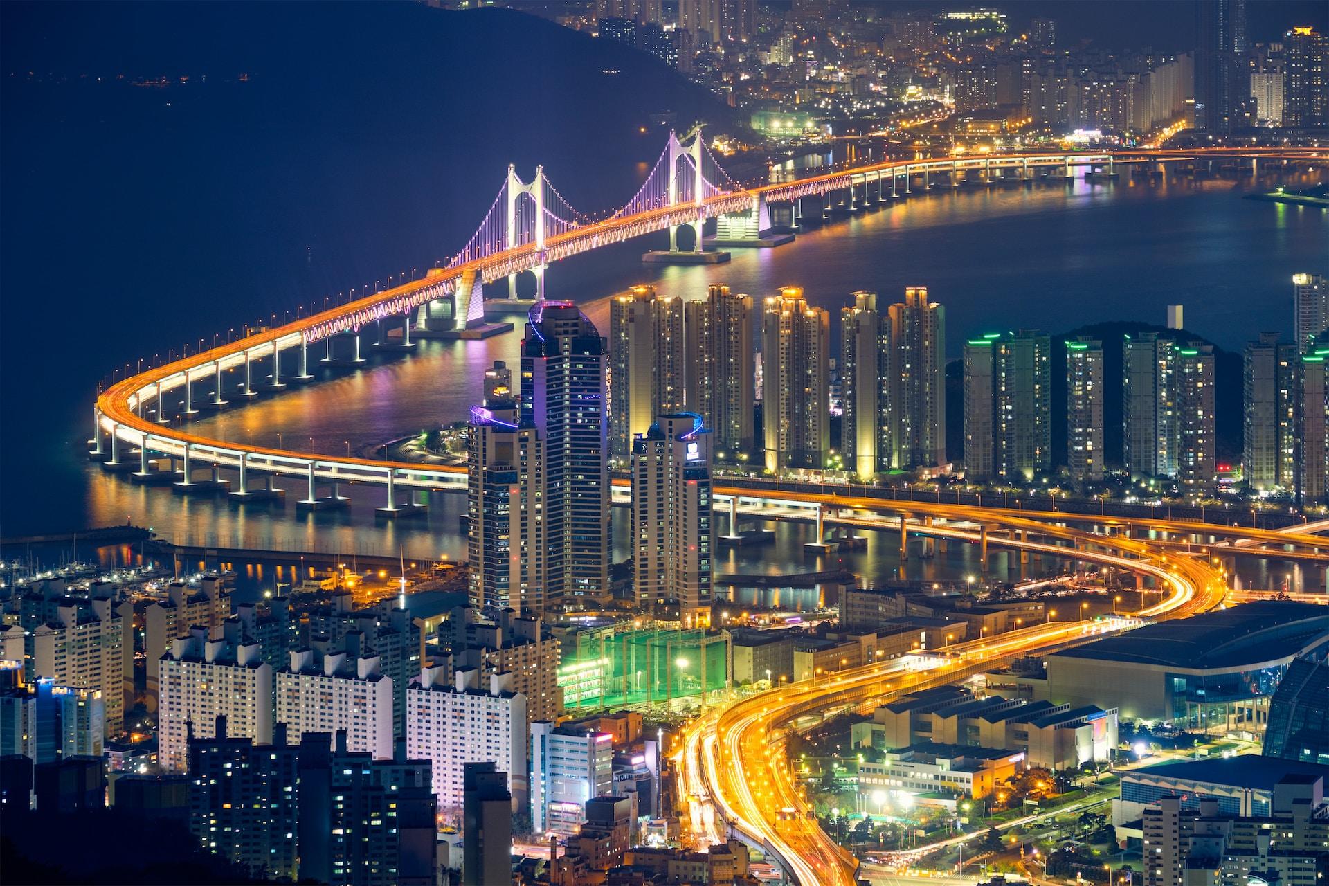 An image of Busan at night, with it's cross-bay bridge lit up and skyscrapers shining.