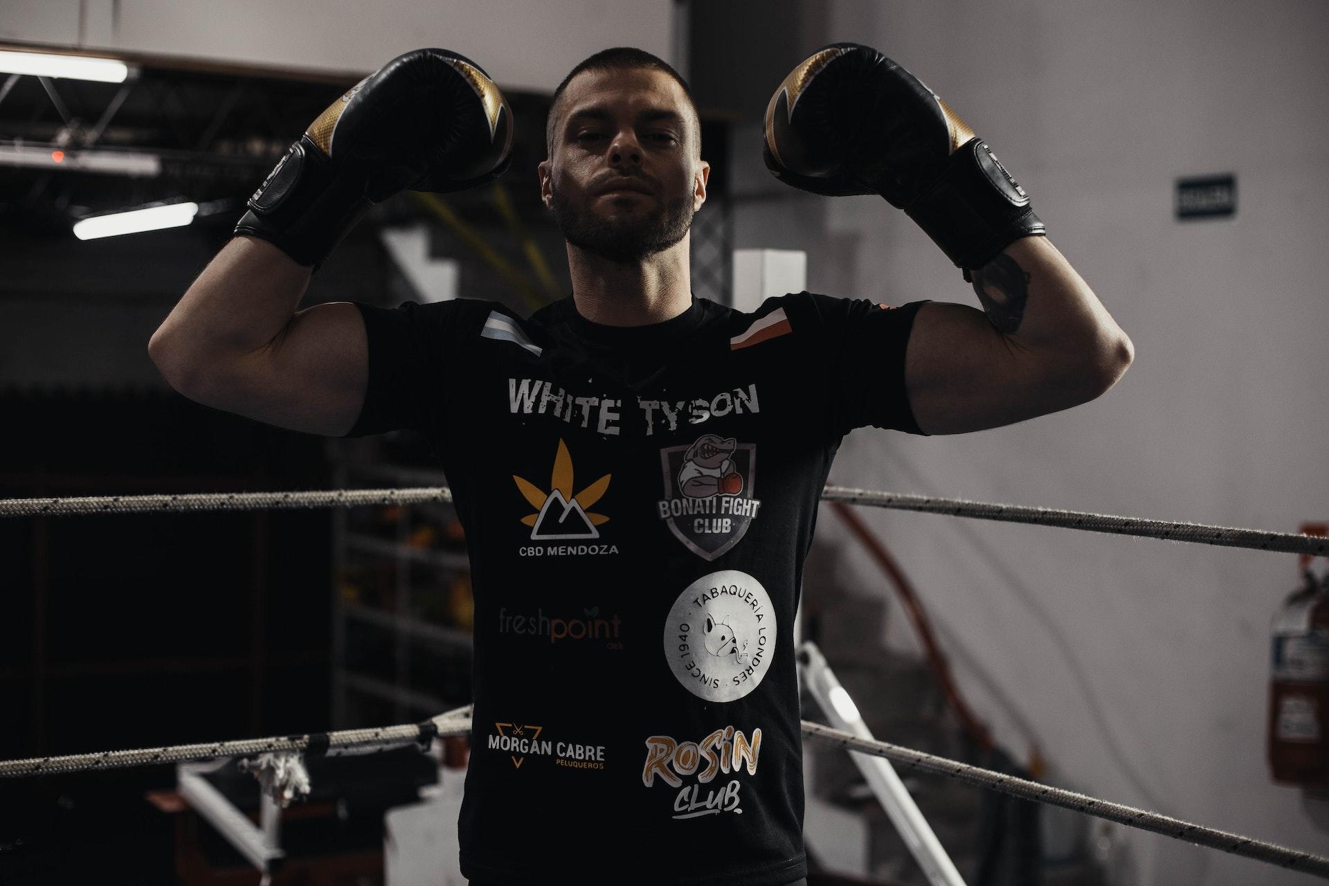 A boxer in a black shirt and gloves flexing his muscles