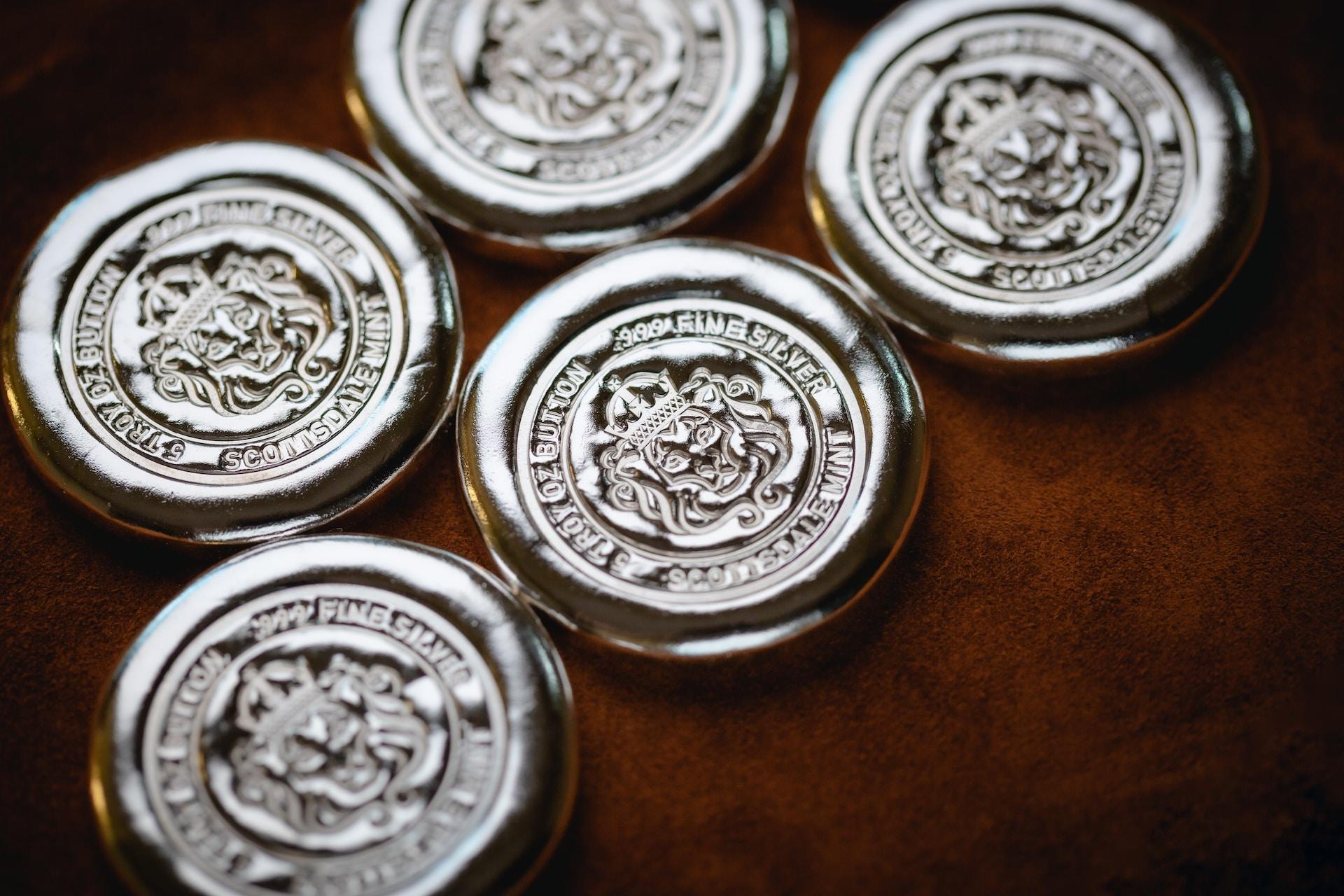 Five silver coins with raised edges and engravings in their centre lay on a dark brown surface.