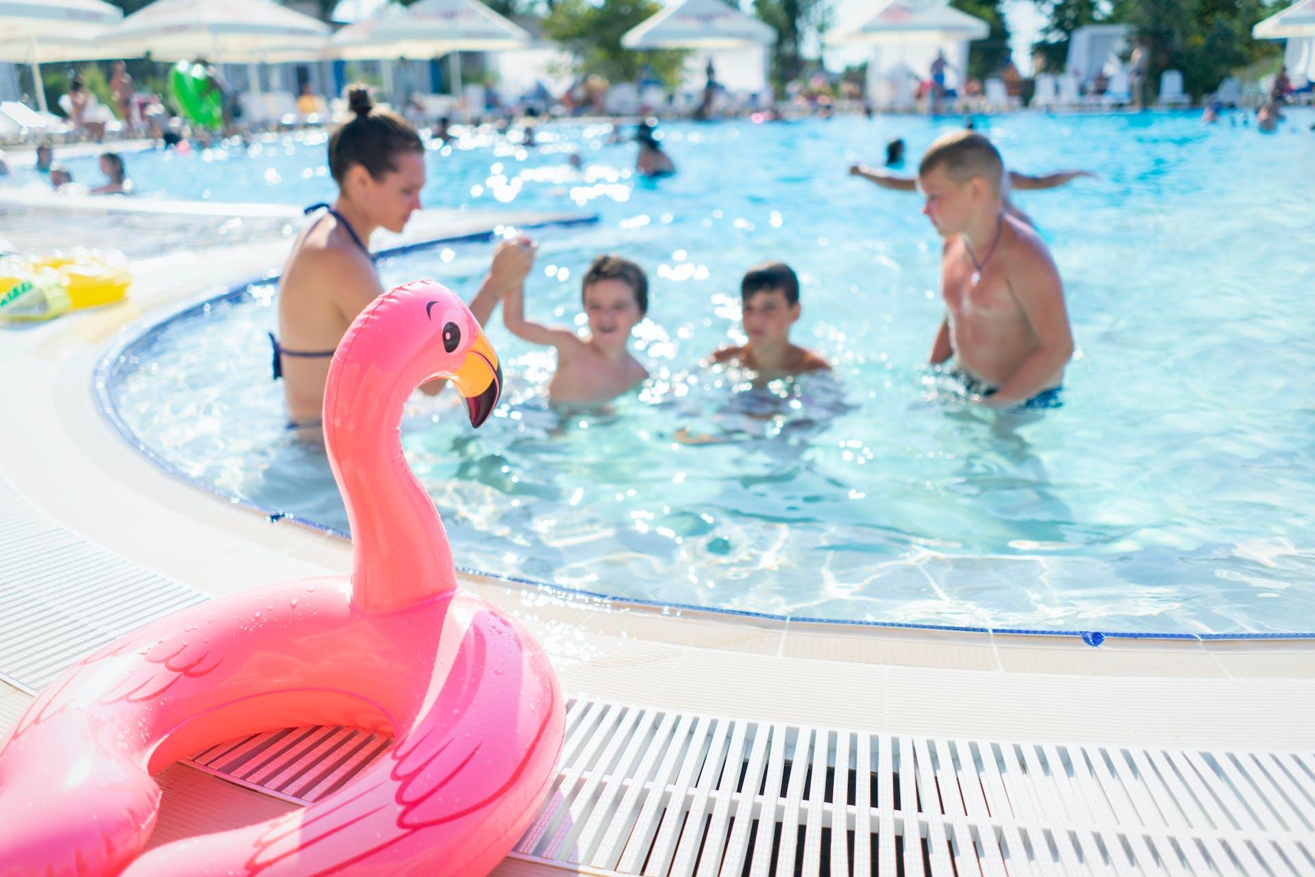A family swims in a beautiful pool while a flamingo float looks on.