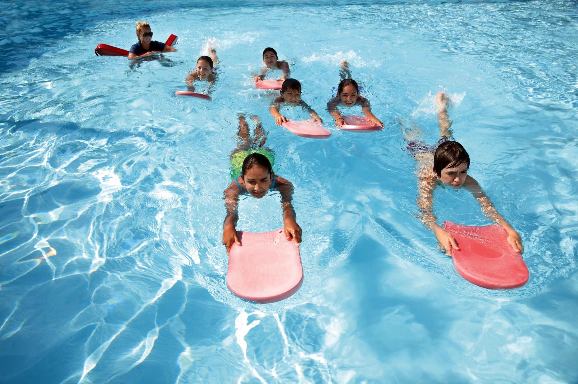 Seven children practicing swimming with kickboards in a pool.