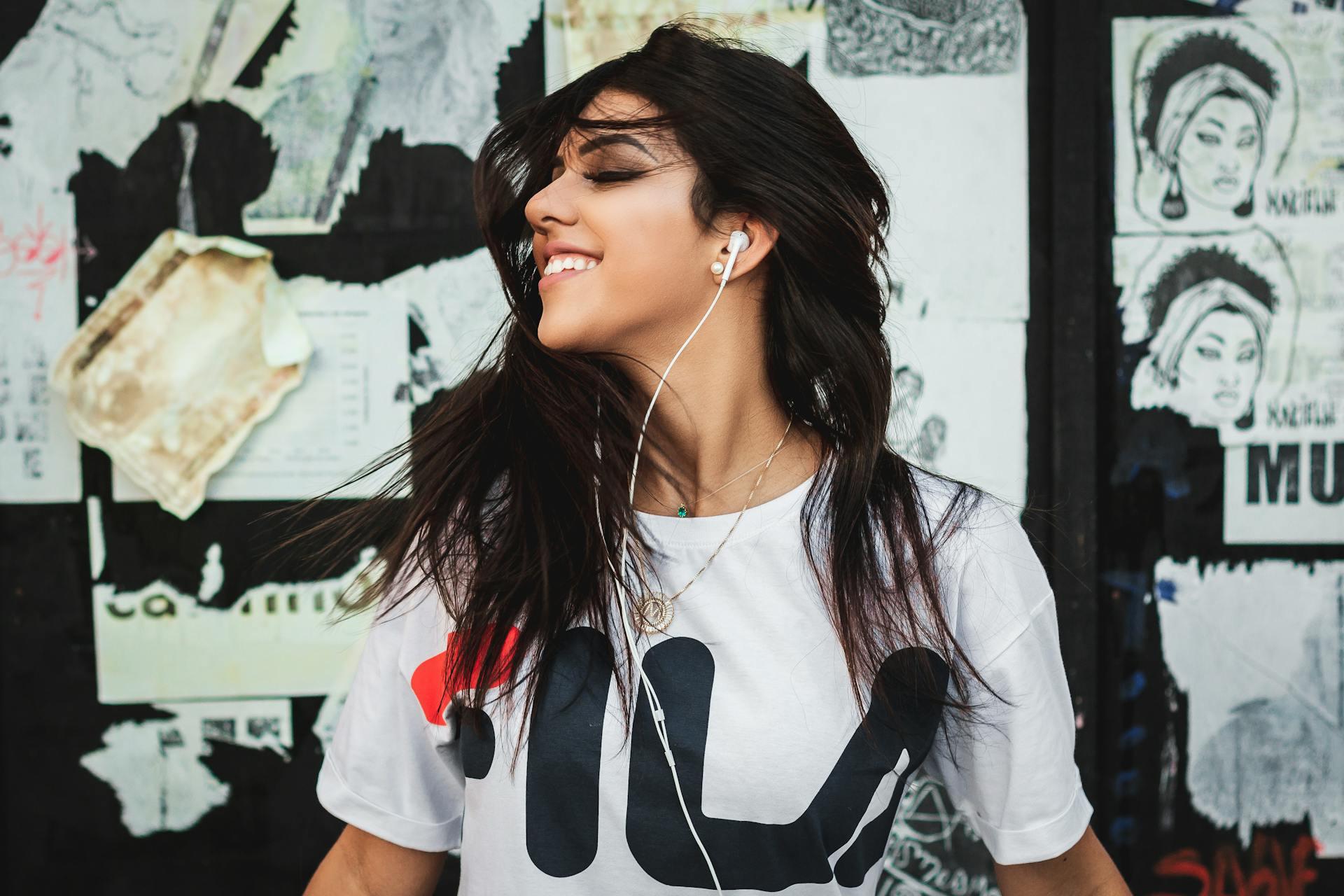 A smiling girl wearing headphones in front of a wall with torn posters